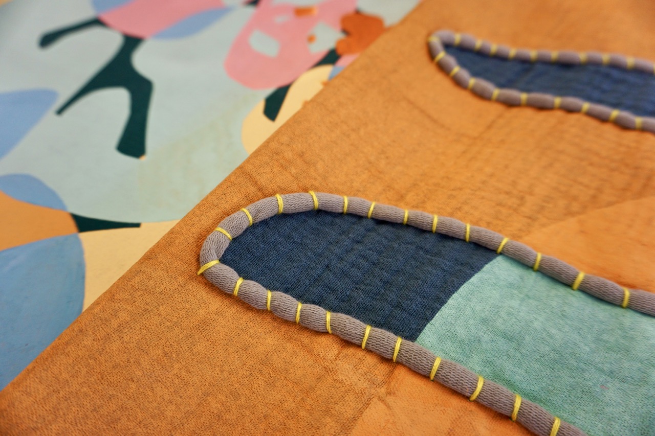 An abstract textile design featuring multiple colours including orange, blue, and pink. Two patterned fabric pieces with contrasting textures and outlines are visible, showcasing a combination of curves and geometric shapes.