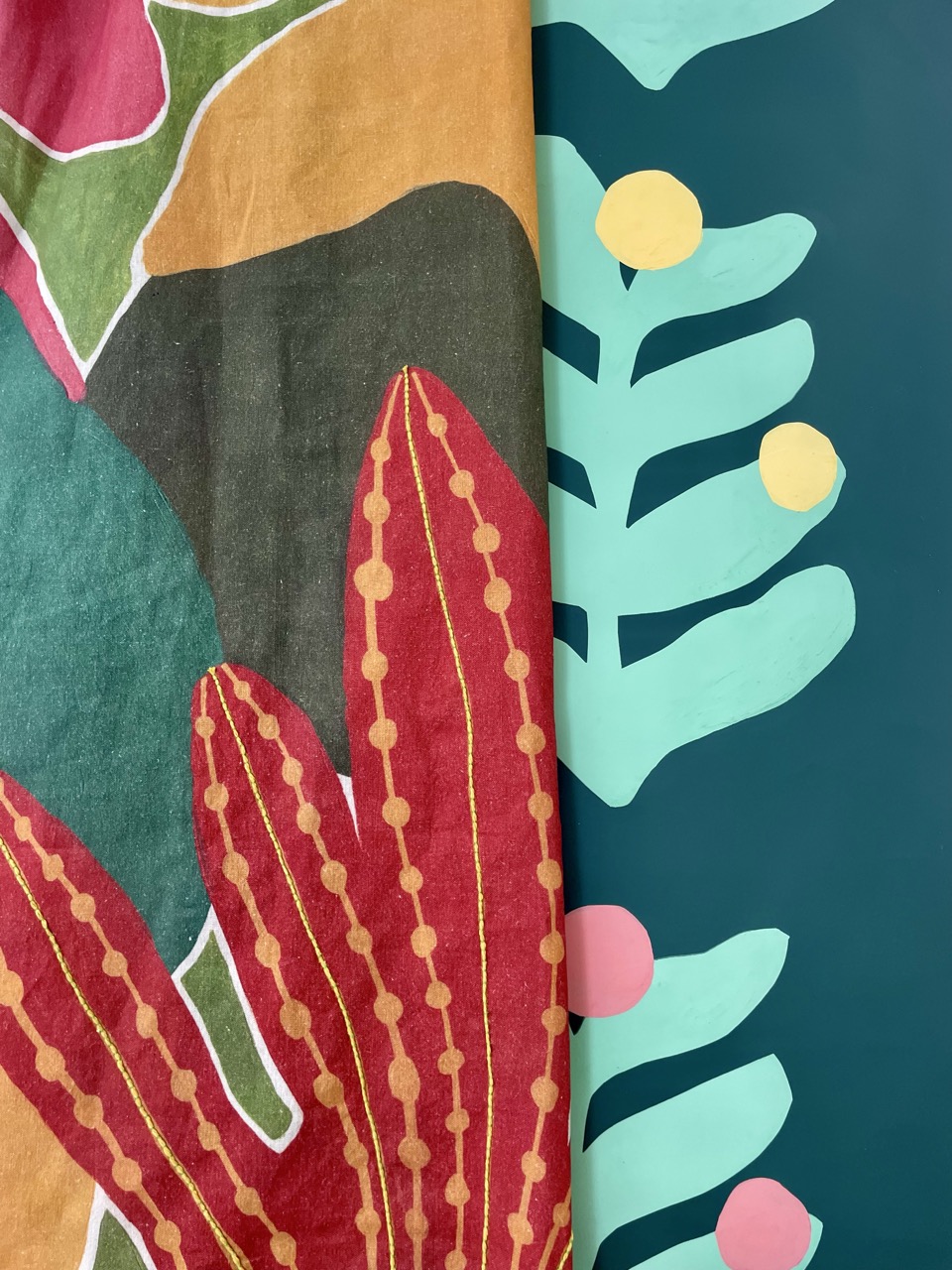 A close-up of two fabric patterns side by side. The left fabric features vibrant red and green abstract plant designs, while the right fabric showcases a teal background with stylised leaf shapes and circular yellow and pink accents.