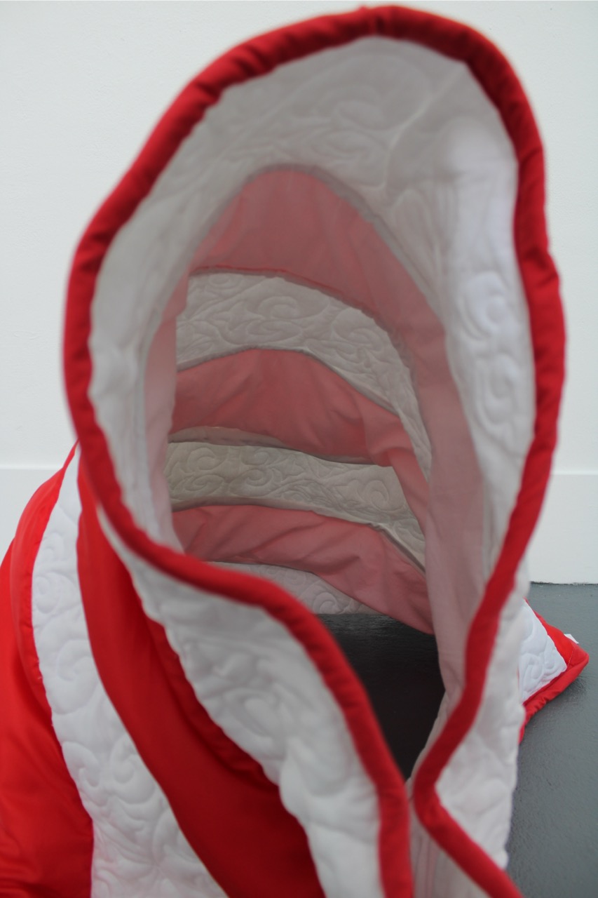 A red and white striped sleeping bag, laid open to show its interior. The quilted lining features alternating sections of white and a lighter shade of red.