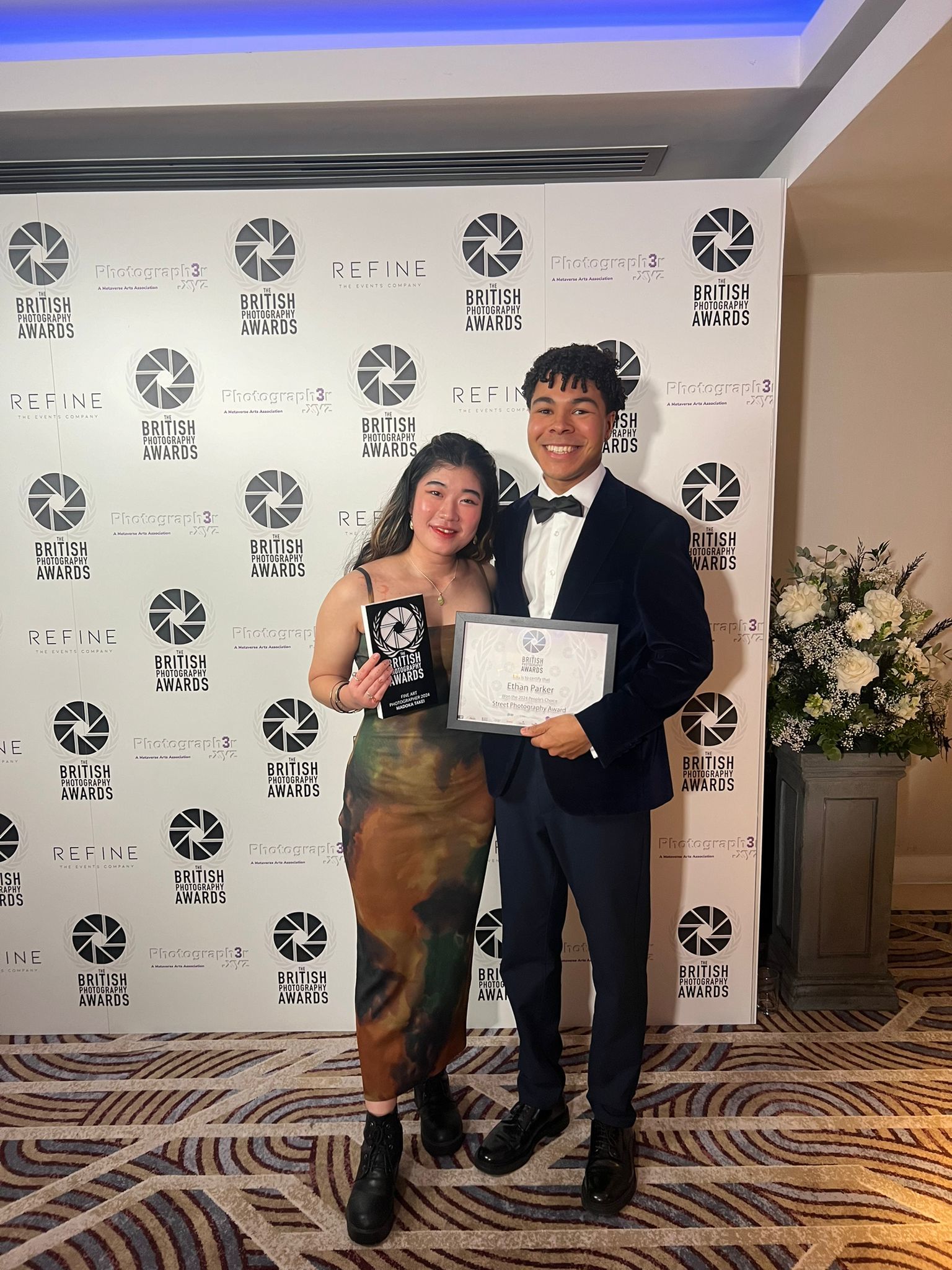 Photographers M Takei and E Parker posing for a photo while holding their awards at the British Photography Awards 2024.