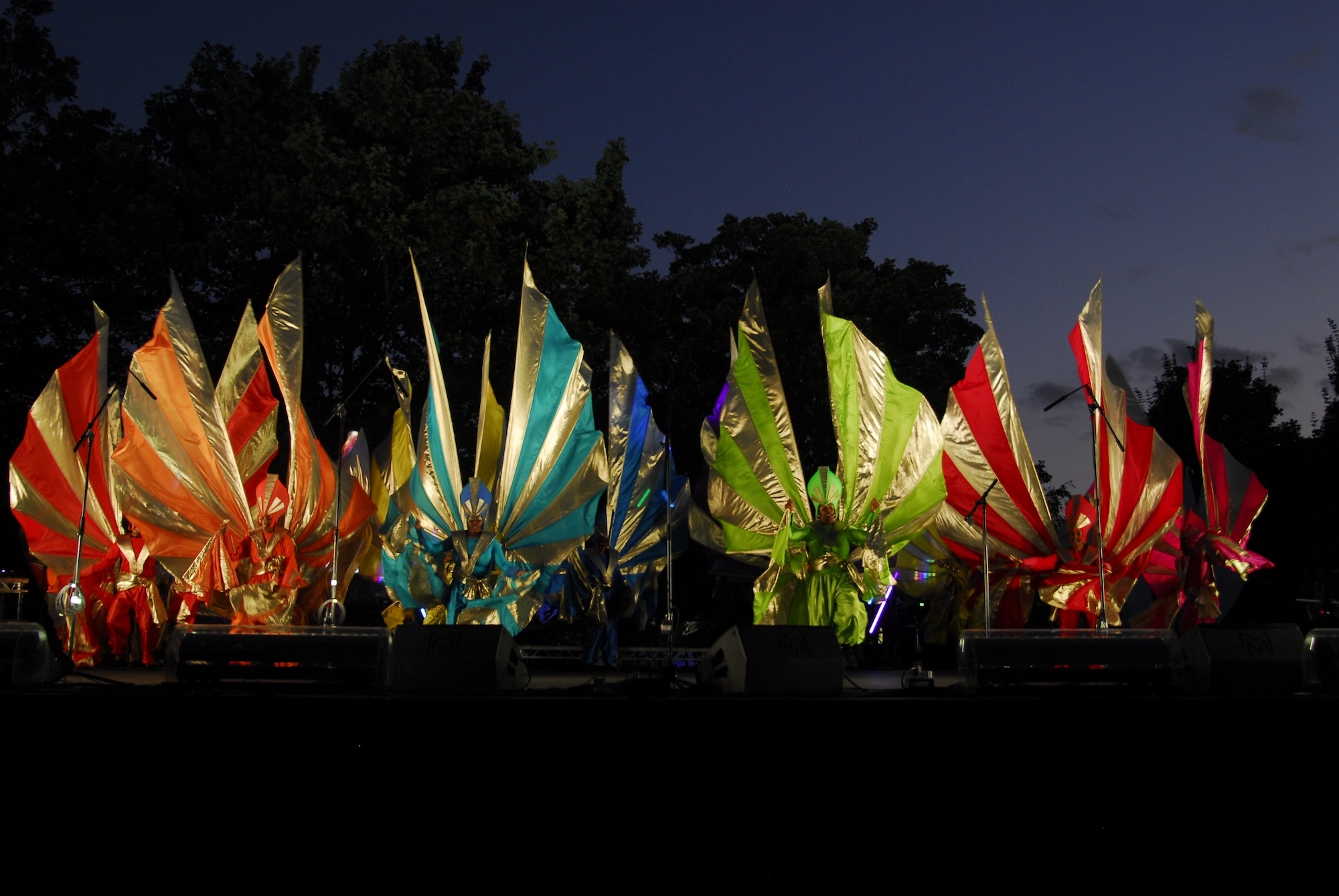 A number of carnival performers in large colourful costumes performing at night.