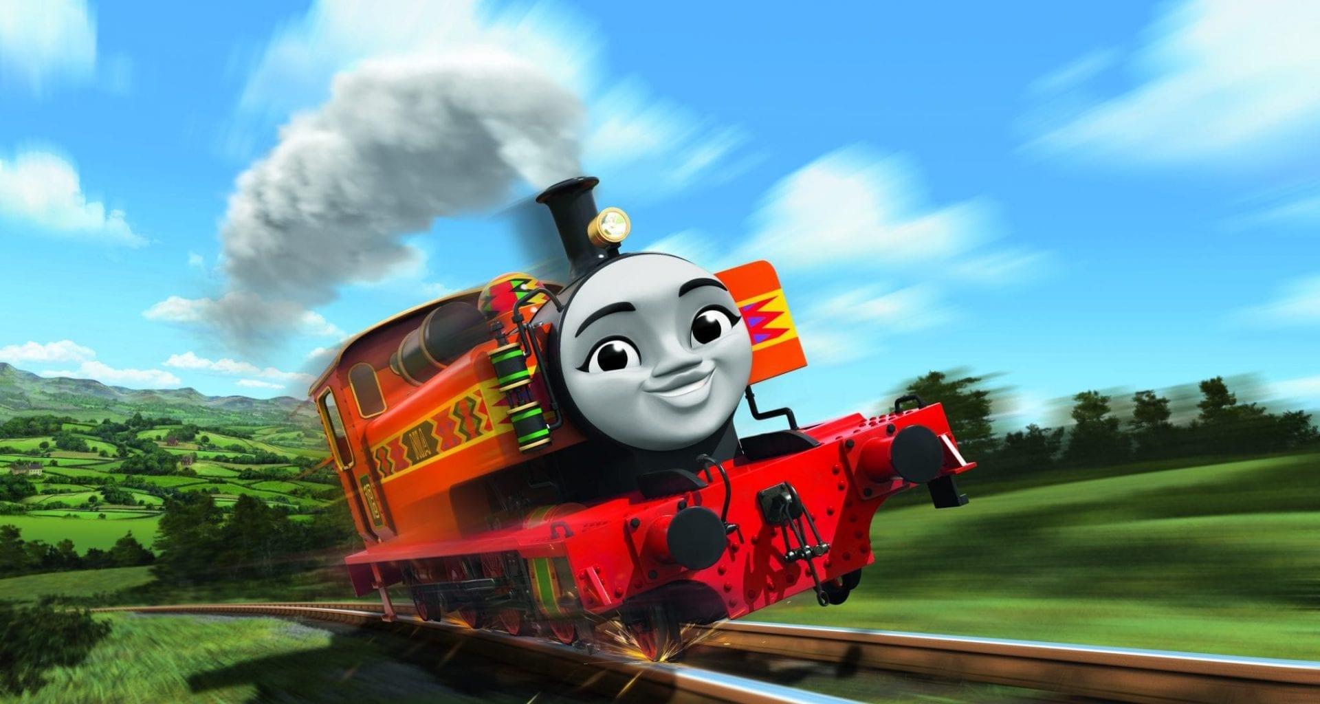 A red-coloured railway engine character with a smiling face travelling on a railway. Fields and trees are shown in the background.