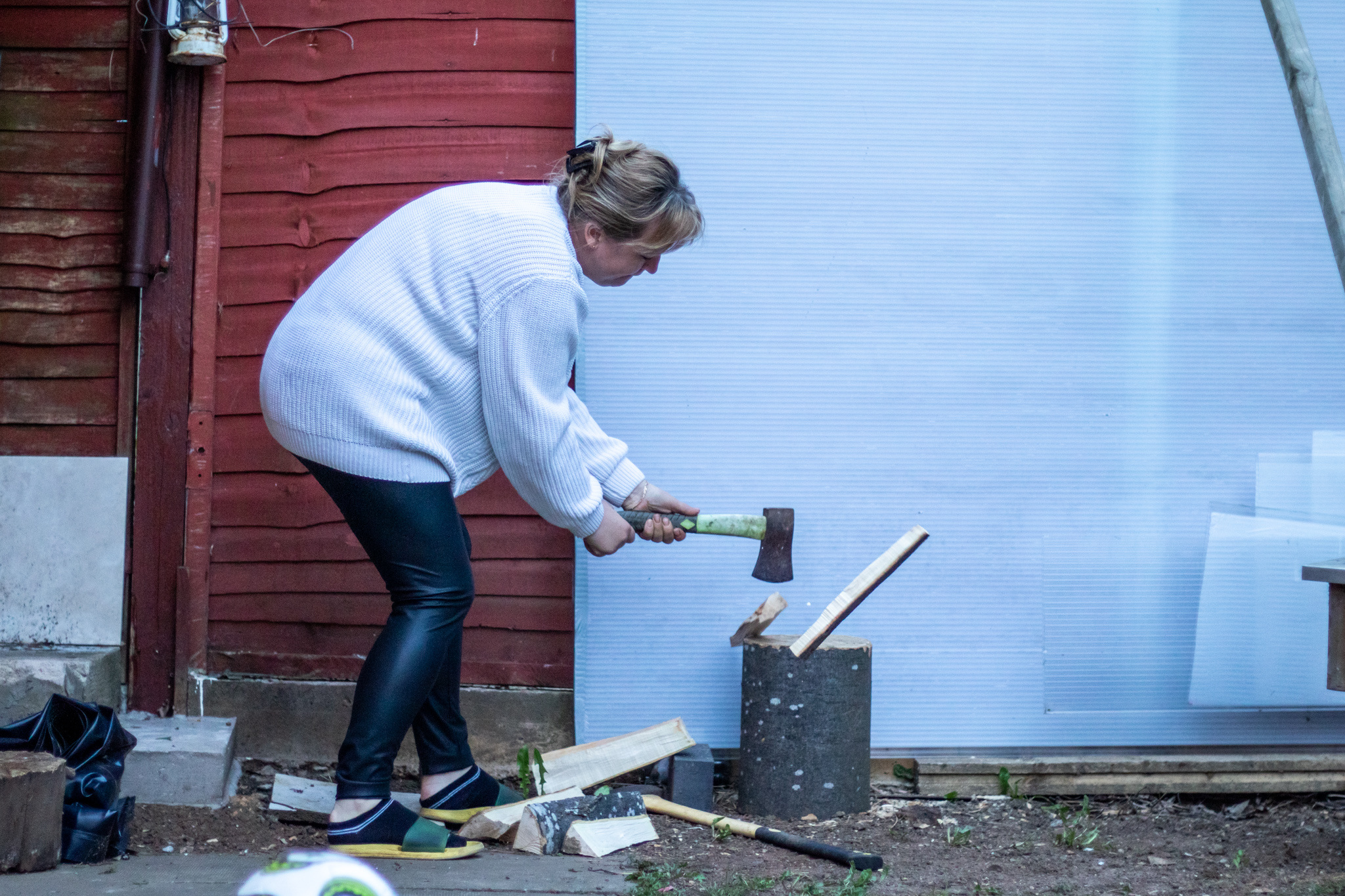 A person in their back yard uses a small axe on a block of wood.