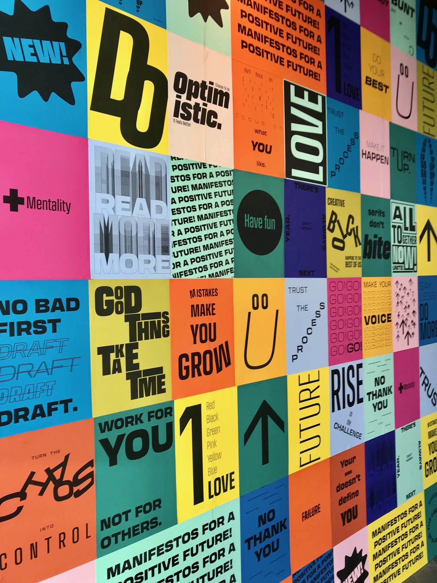 A series of colourful adverts and posters arranged on a wall viewed at a diagonal.