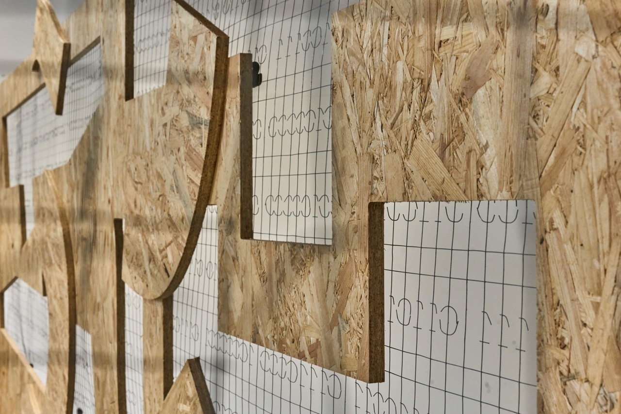 Wooden templates and grid paper patterns pinned to chipboard wall, showing curved and angular shapes for crafting or design work.