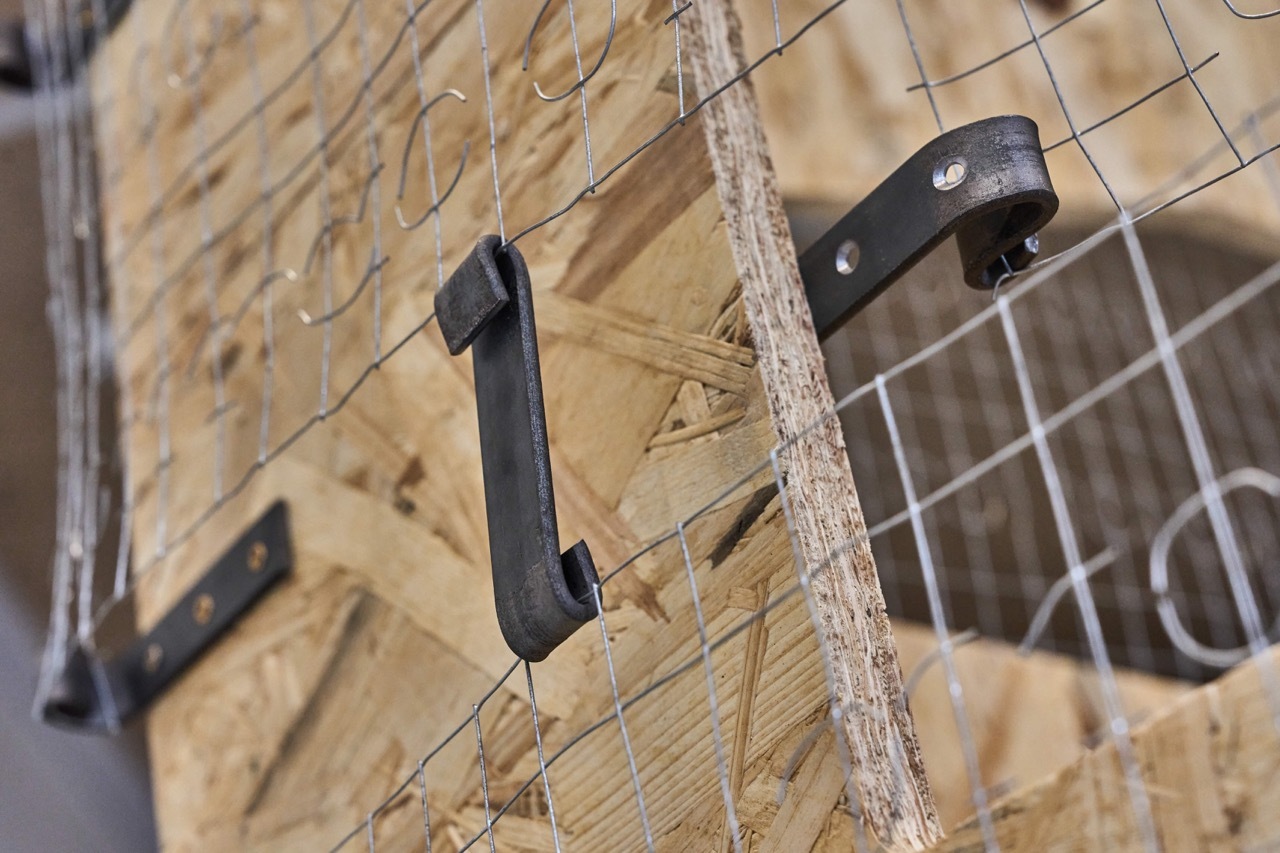 Black handled knife with serrated blade attached to wire mesh cage against wooden background.