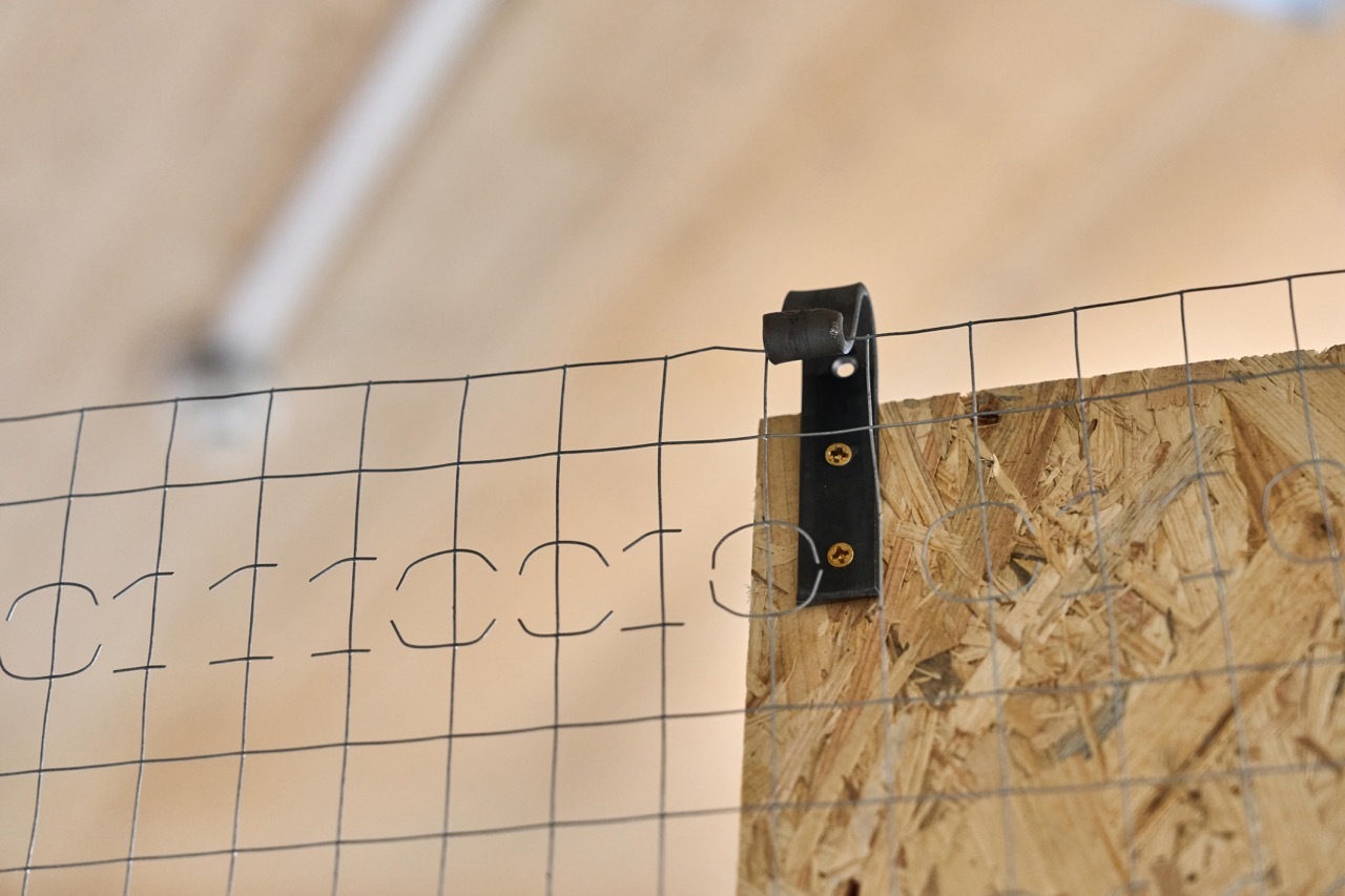 Black measuring device attached to wire grid above wooden surface with measurement markings visible on grid.