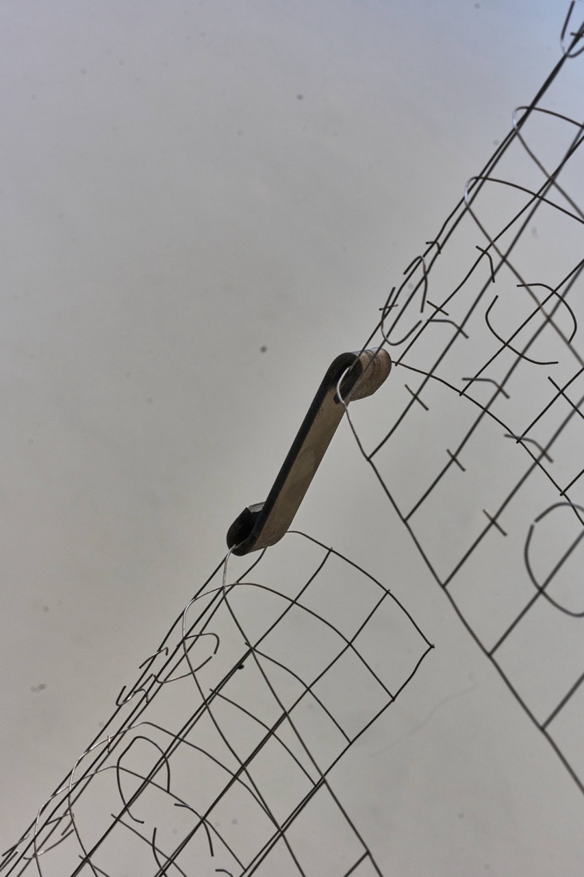 Black metal pole mounted on wire fence against overcast grey sky, viewed from below at diagonal angle.