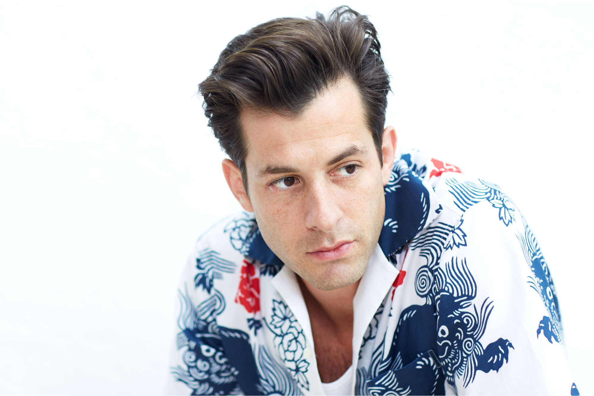 Man with dark hair wearing white shirt with blue and red floral pattern, looking directly at camera against white background.