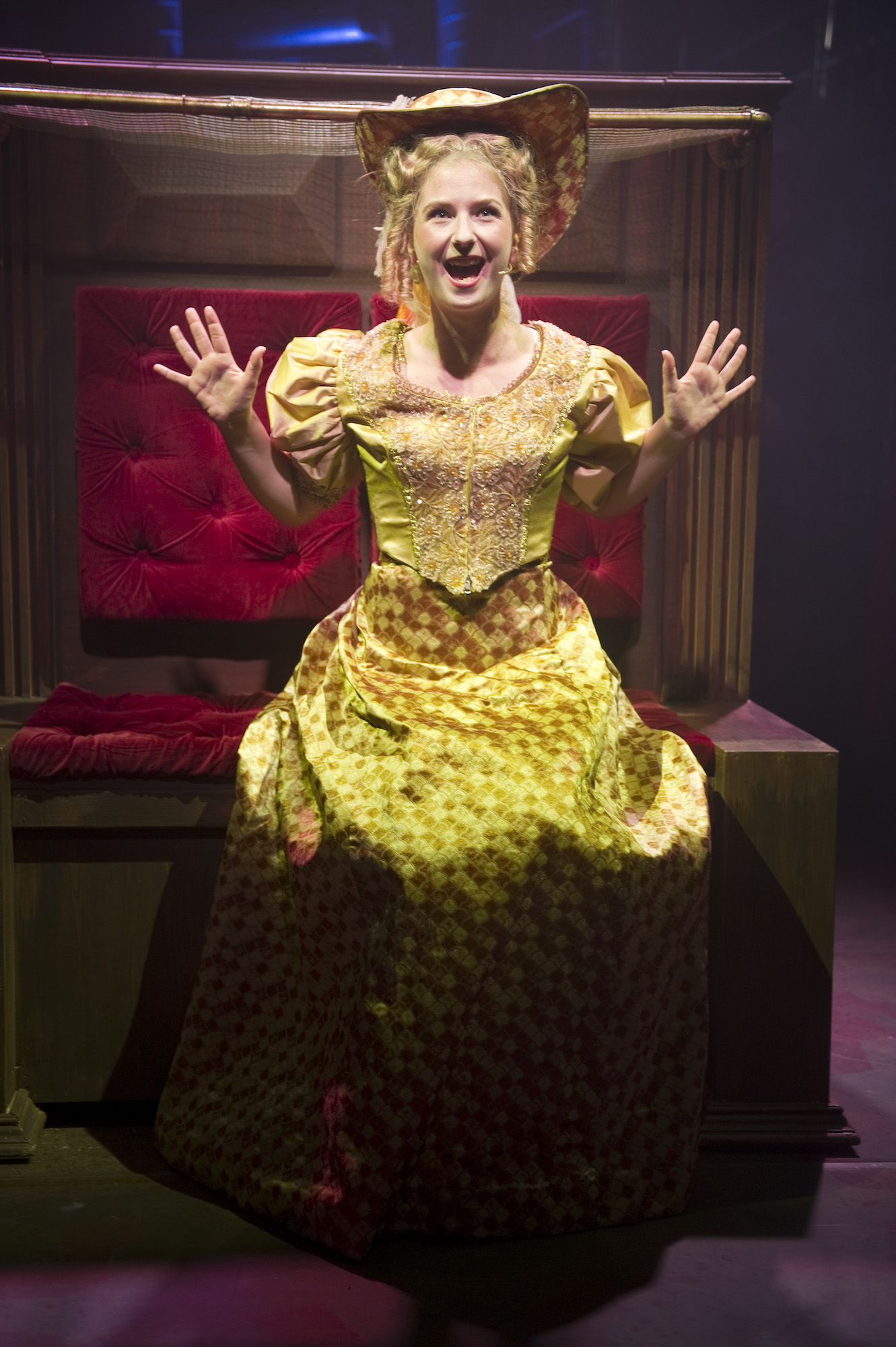A BA (Hons) Acting student in a ballgown holds their hands up looking excited.