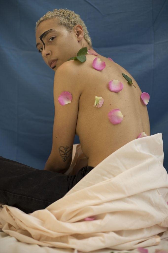 Shirtless model sitting looking over their shoulder with flower petals on their back.