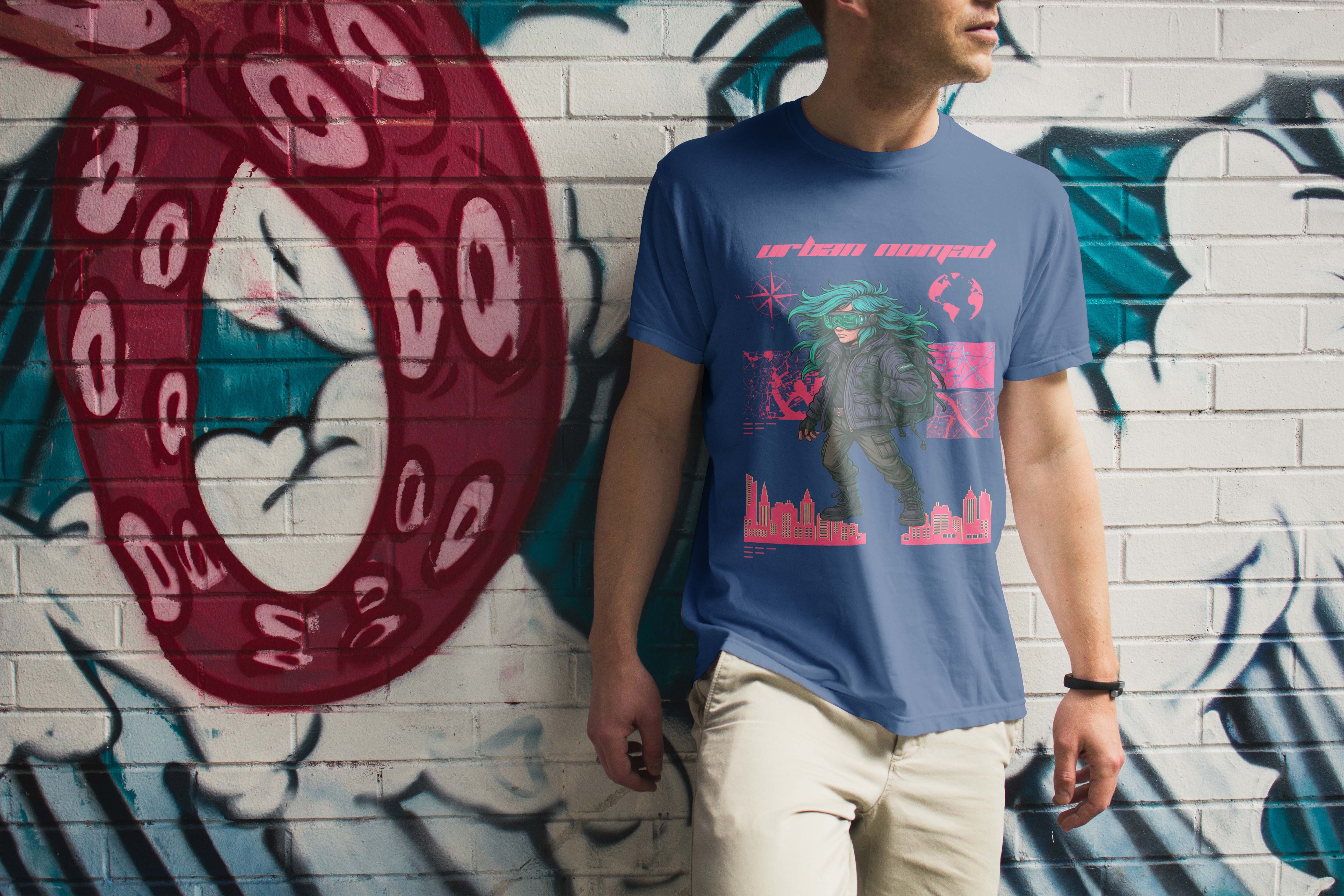 Person in blue t-shirt with pink and green graphic design standing against white brick wall with red, teal and black graffiti.