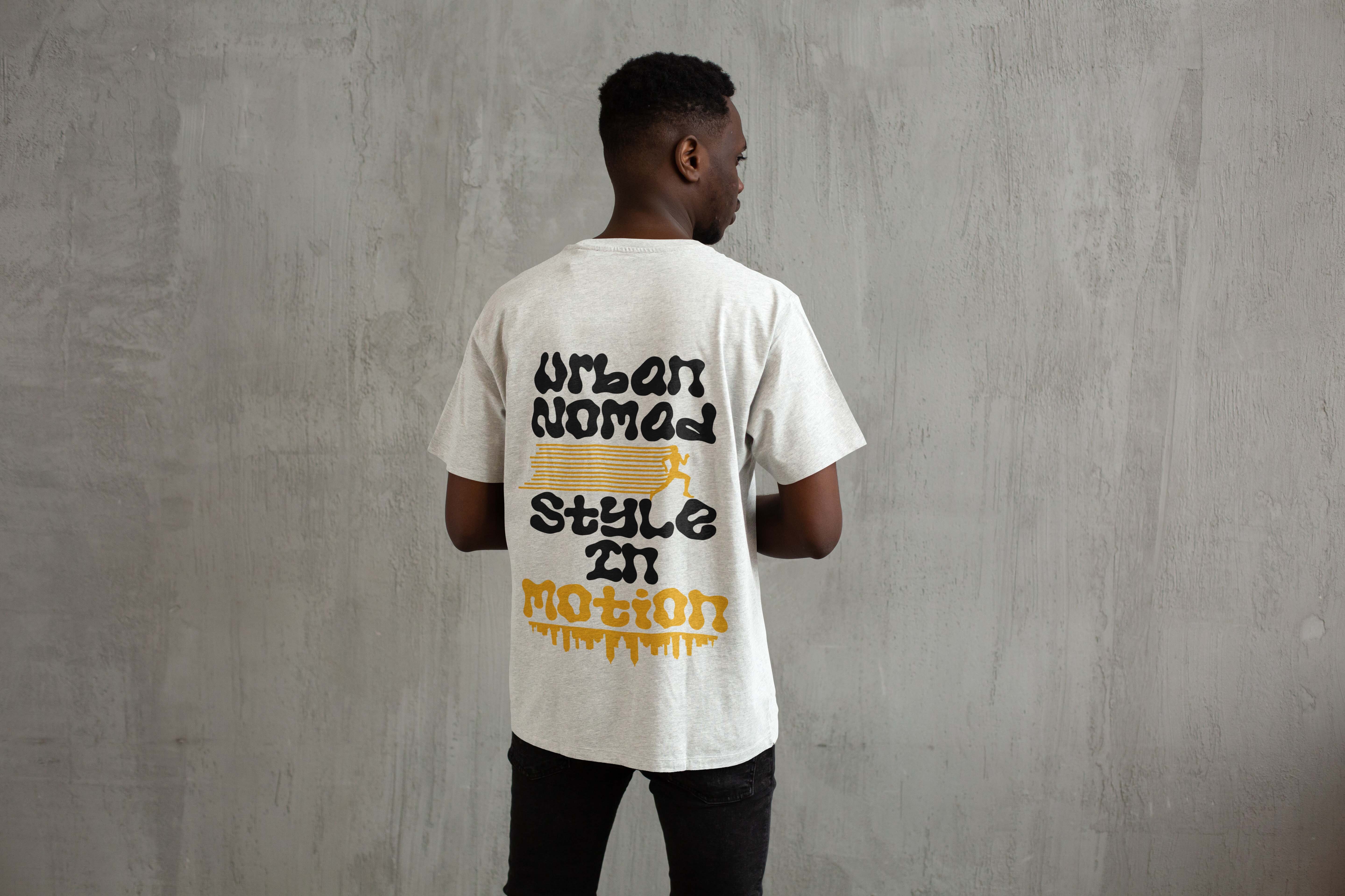 Man wearing white t-shirt with black and yellow text reading "URBAN JUNGLE STYLE" standing against grey concrete wall, viewed from behind.