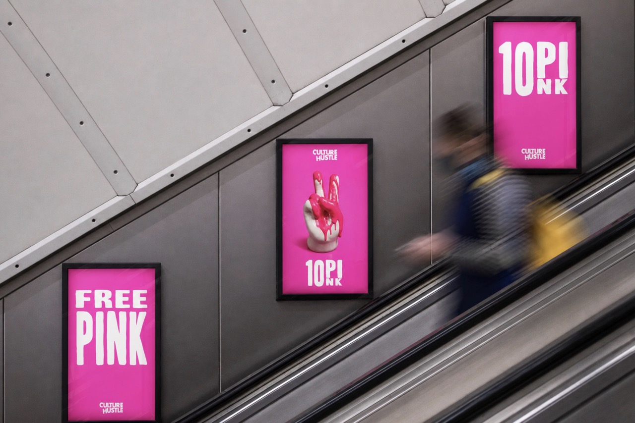 A blurred figure descends an escalator beside three framed advertisements on a pink background. The left ad displays the text 'FREE PINK,' the central ad features a stylised image of a hand, and the right ad states '10 PINK.'