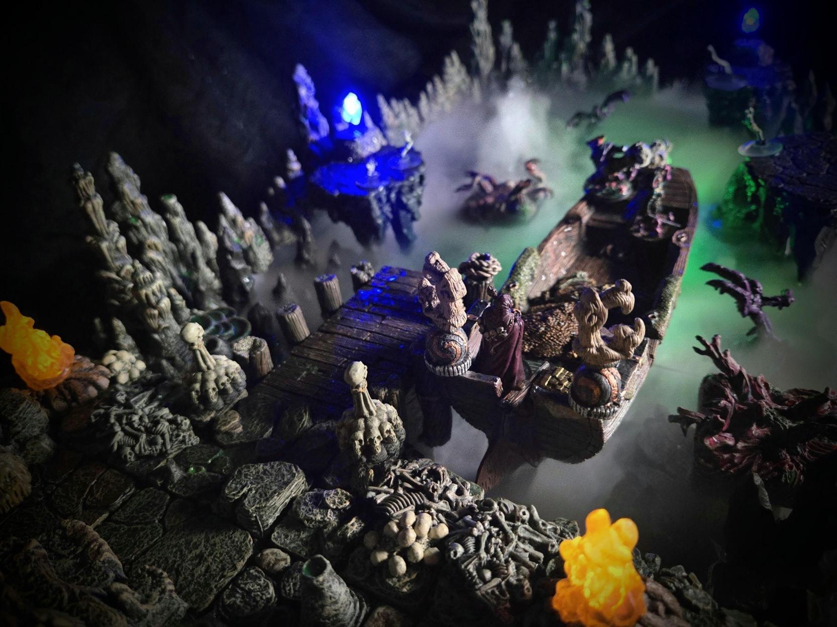 A fantasy tabletop game diorama shows a narrow wooden bridge over a misty chasm, surrounded by carved stone figures, clusters of mushrooms and glowing blue and orange lights.