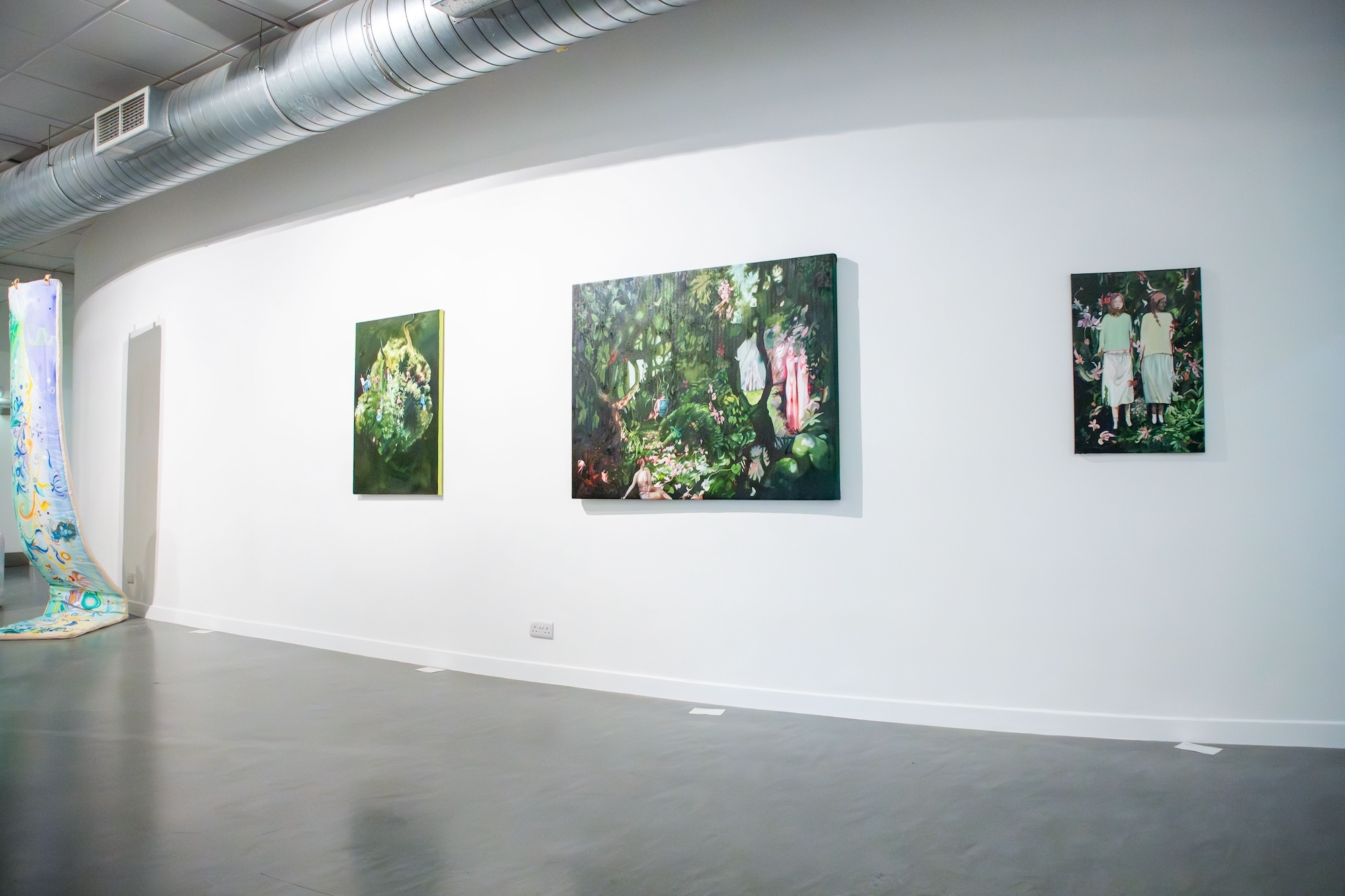 Three paintings of floral images, two on rectangular canvases, the centre on a square canvas, all on display on a gallery wall.