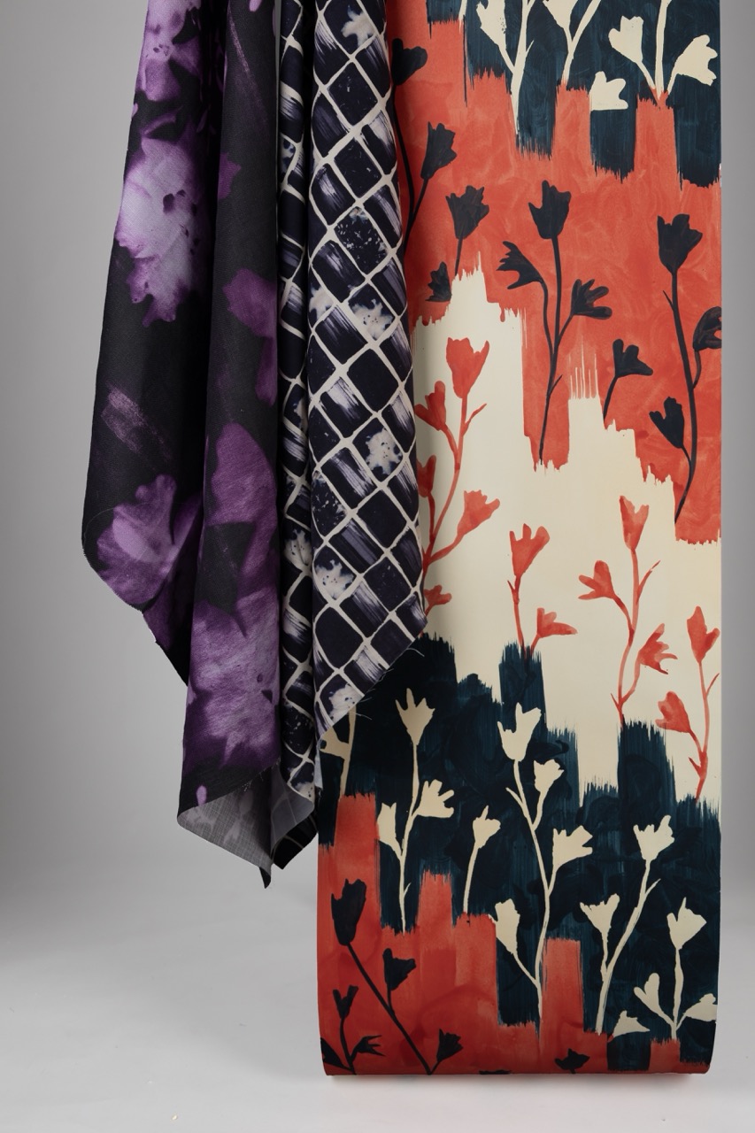 Three pieces of fabric arranged together. The first is a sheer purple fabric with a abstract pattern, the second is a plaid design in navy and white, and the third features a floral print in red, black, and cream colours.