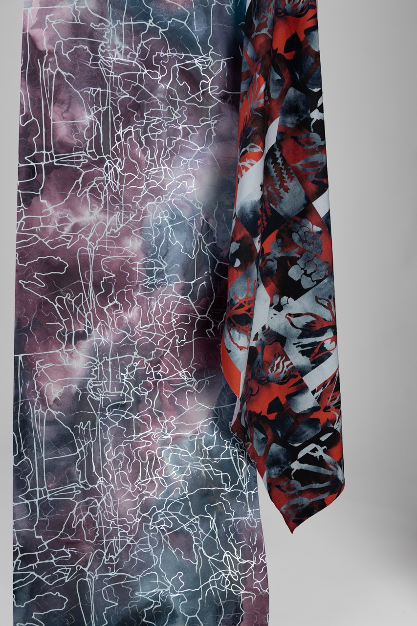 A long scarf featuring a combination of two designs: one side has a purple and grey abstract pattern with white line drawings, while the other side displays a vibrant red and black geometric pattern with floral elements.