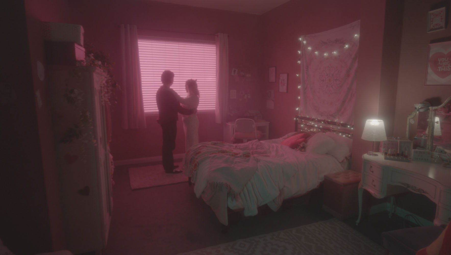 Two silhouetted figures standing near a window with bright pink light flooding a bedroom containing a bed, desk, and string lights.