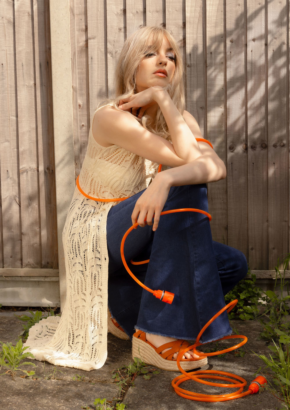 Female model in a garden, partly in the sun, partly in the shade, with a hosepipe wrapped around her legs.