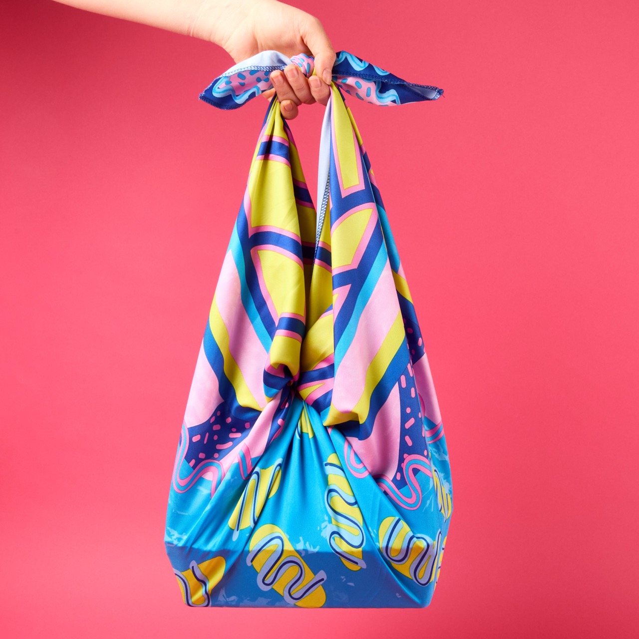 Multicoloured, pattered Lush Knot Wrap on a bright coral pink/red background.