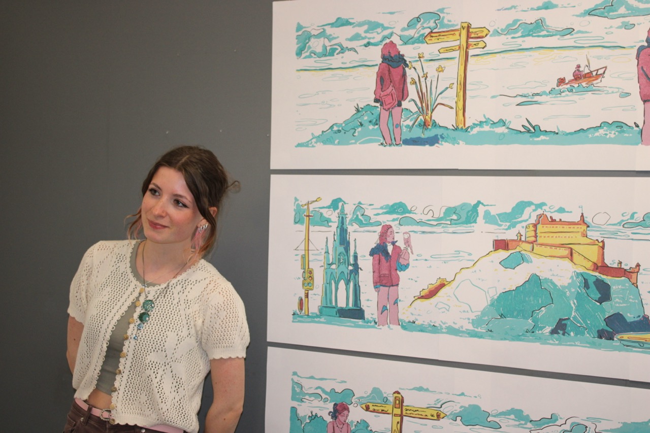 A woman with dark hair stands beside three framed landscape illustrations on a grey wall.