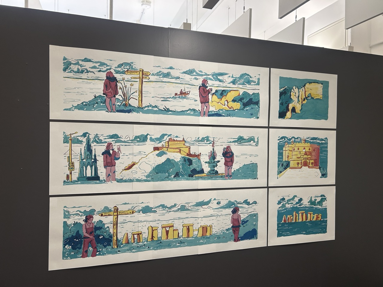 A display wall with six framed coastal landscape prints in a 3-by-2 grid, showing figures, boats and landmarks in blue, yellow and pink tones.
