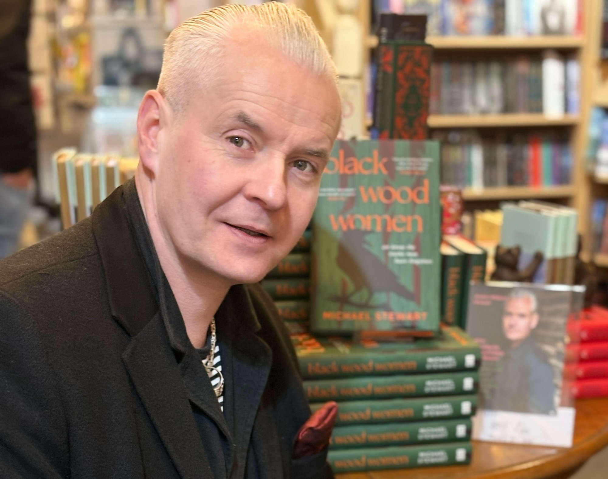 Headshot of M Stewart with copies of his book 'Black Wood Women' in the background.