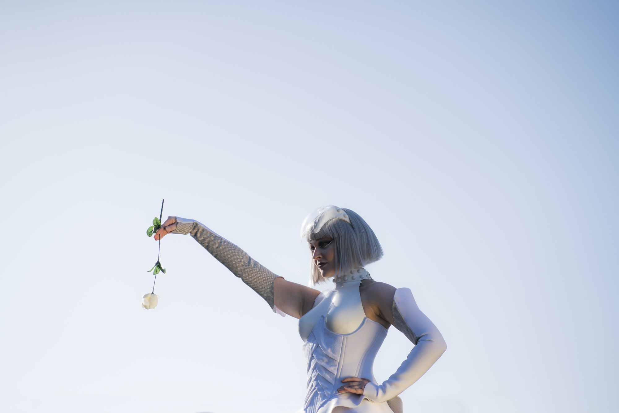 A model in a Hunger Games-inspired costume stands with one hand on their hip and the other held out with a rose in their hand.
