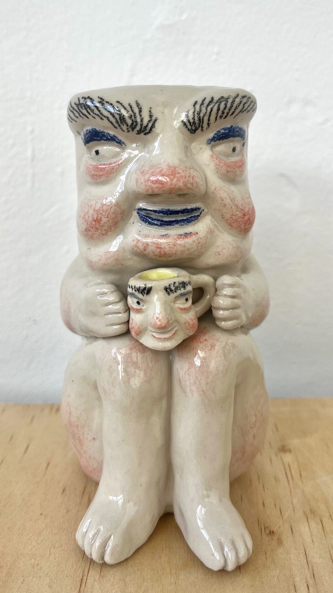 Ceramic figurine with a large face and legs holding a mug of the same appearance, white background.