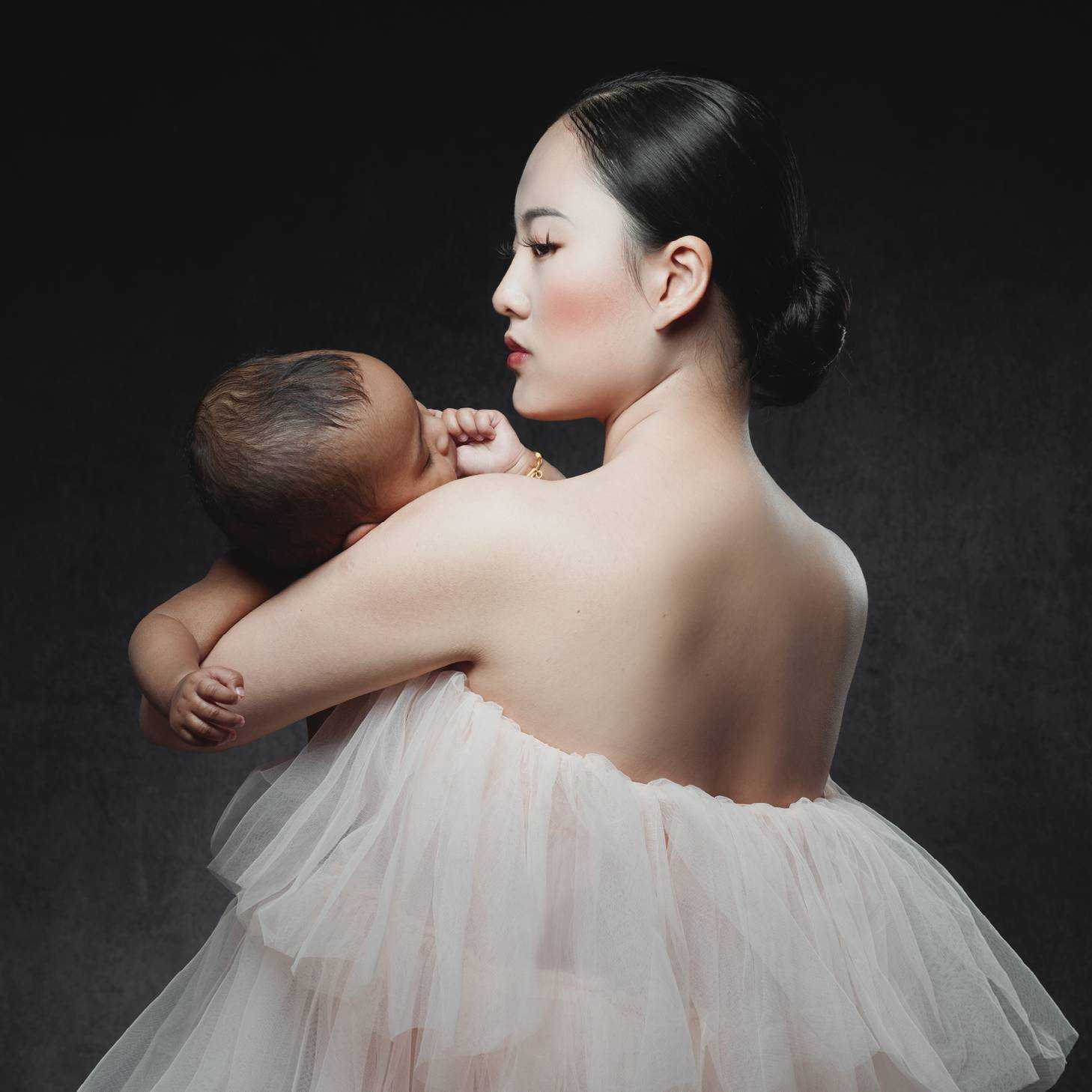 A woman in a backless garment is photographed side-on with a baby in their arms.