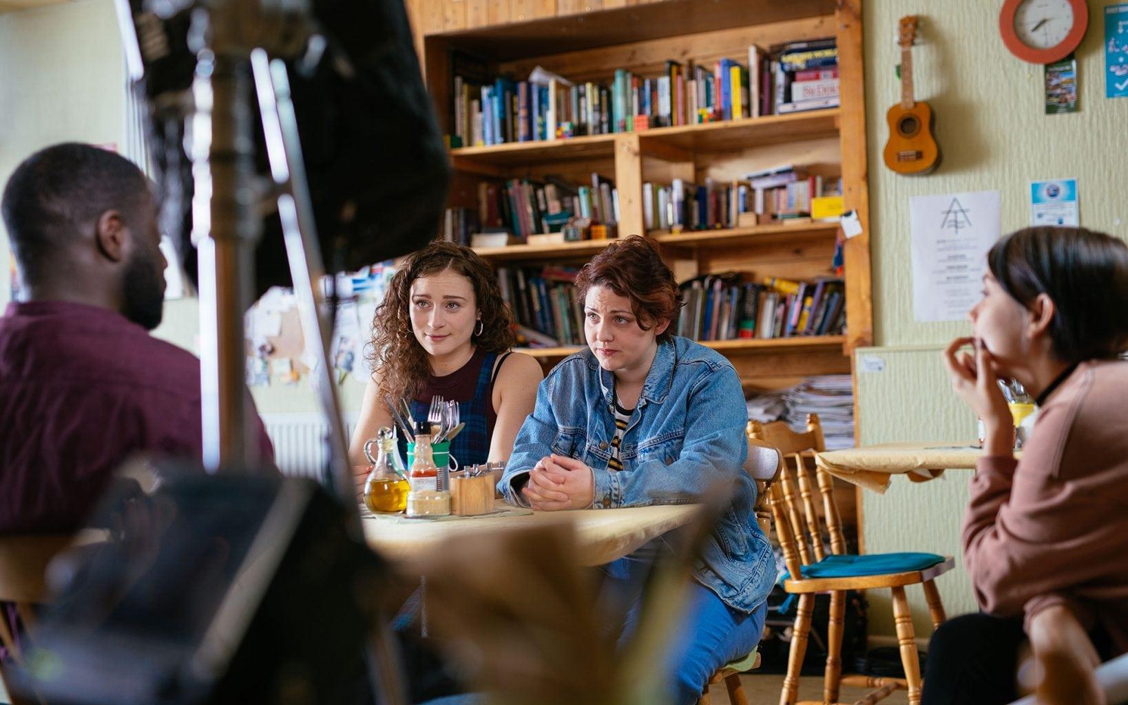 Group of people around a dining room table being filmed.