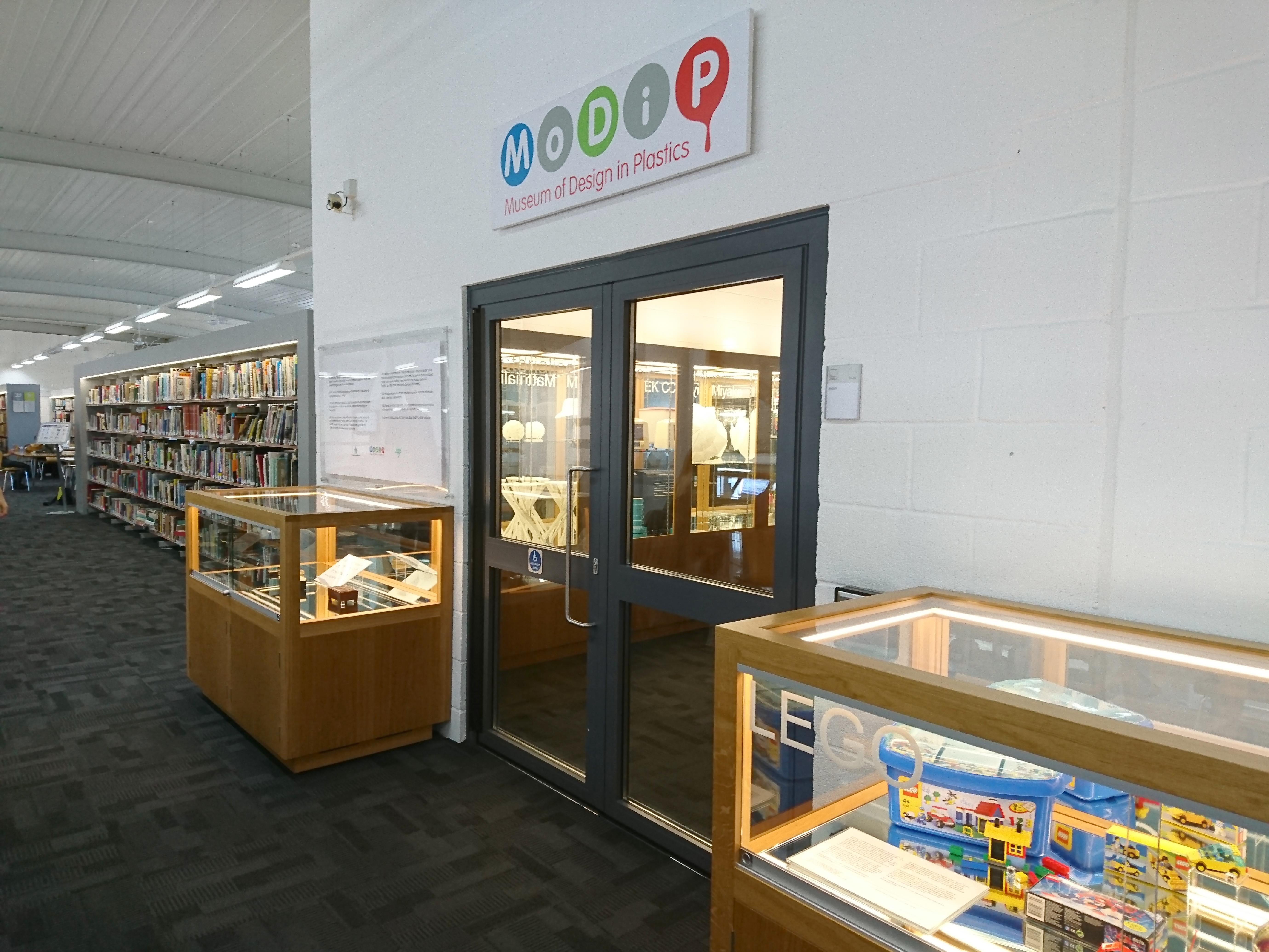 A pair of double doors with a wood and glass display cabinet either side. There is a sign above the door with the name "MoDiP" on it.