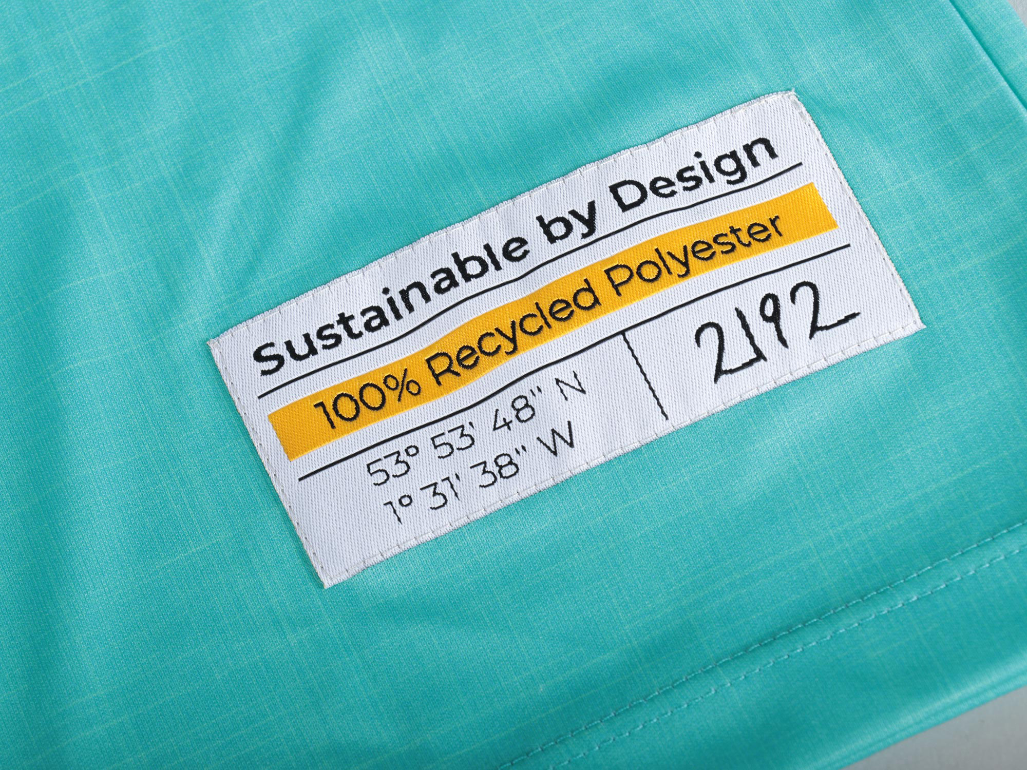 Close-up of a clothing label reading, "Sustainable by Design 100% Recycled Polyester".
