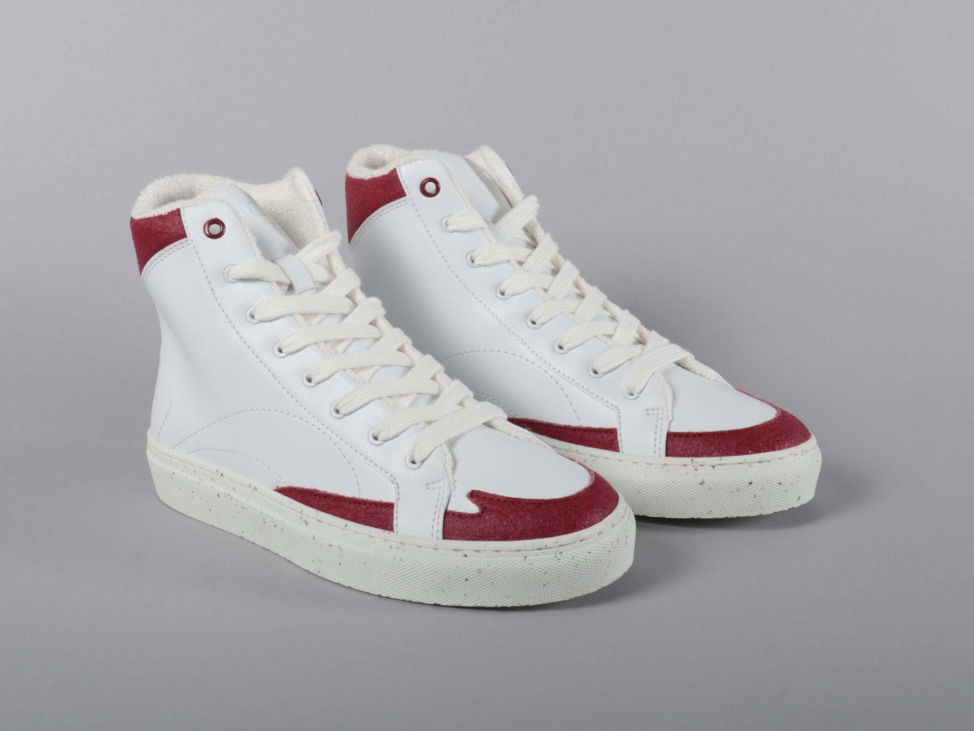 A pair of red and white high-top trainers on a plain background and surface.