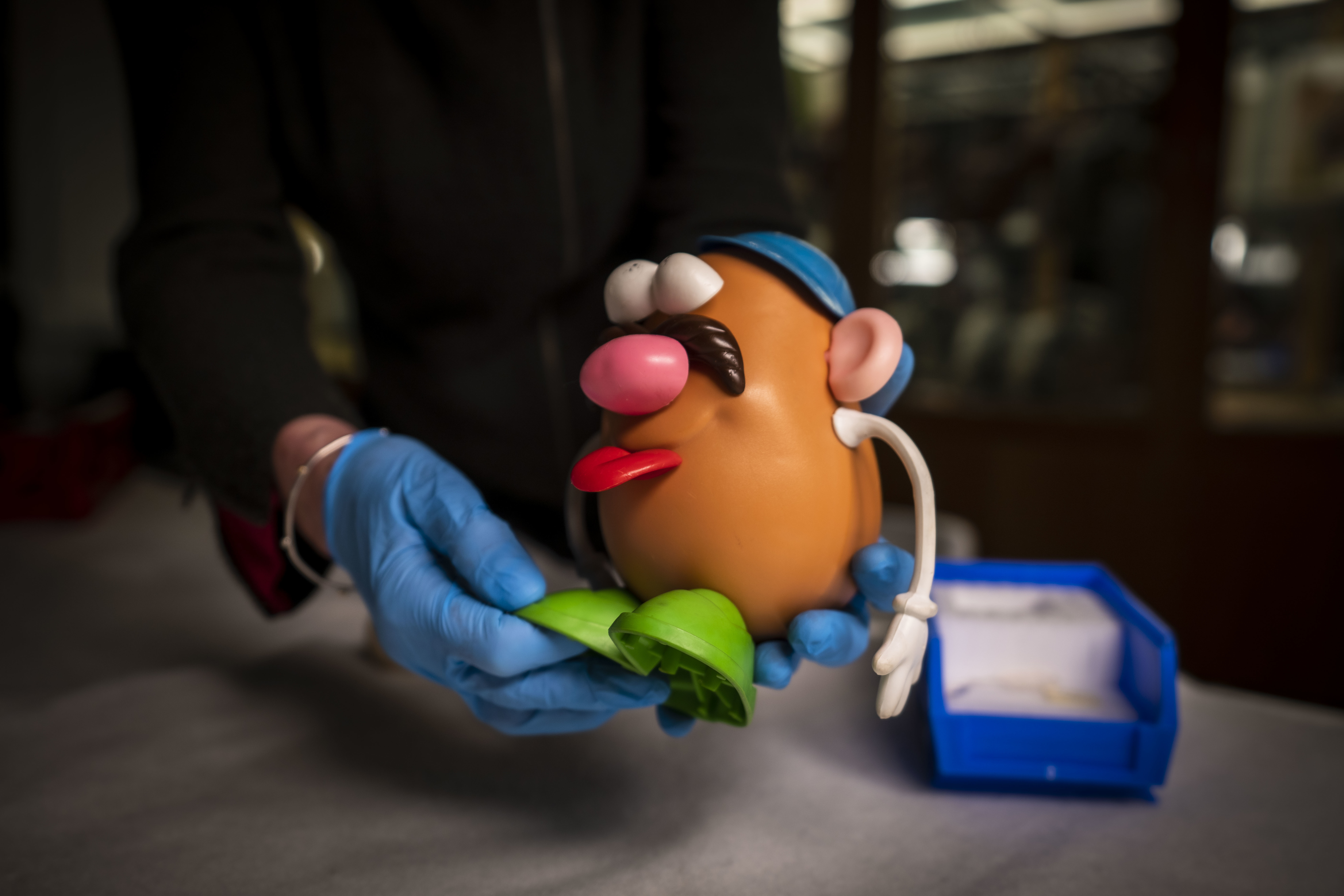 Someone wearing disposable gloves handles an assembled Mr Potato Head toy.