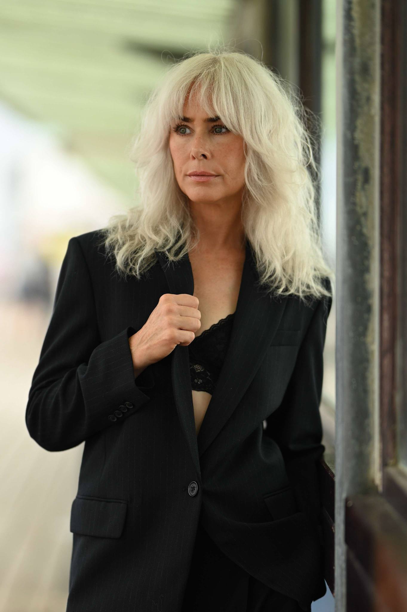 A blonde model wearing a black blazer with a black bra partly exposed.