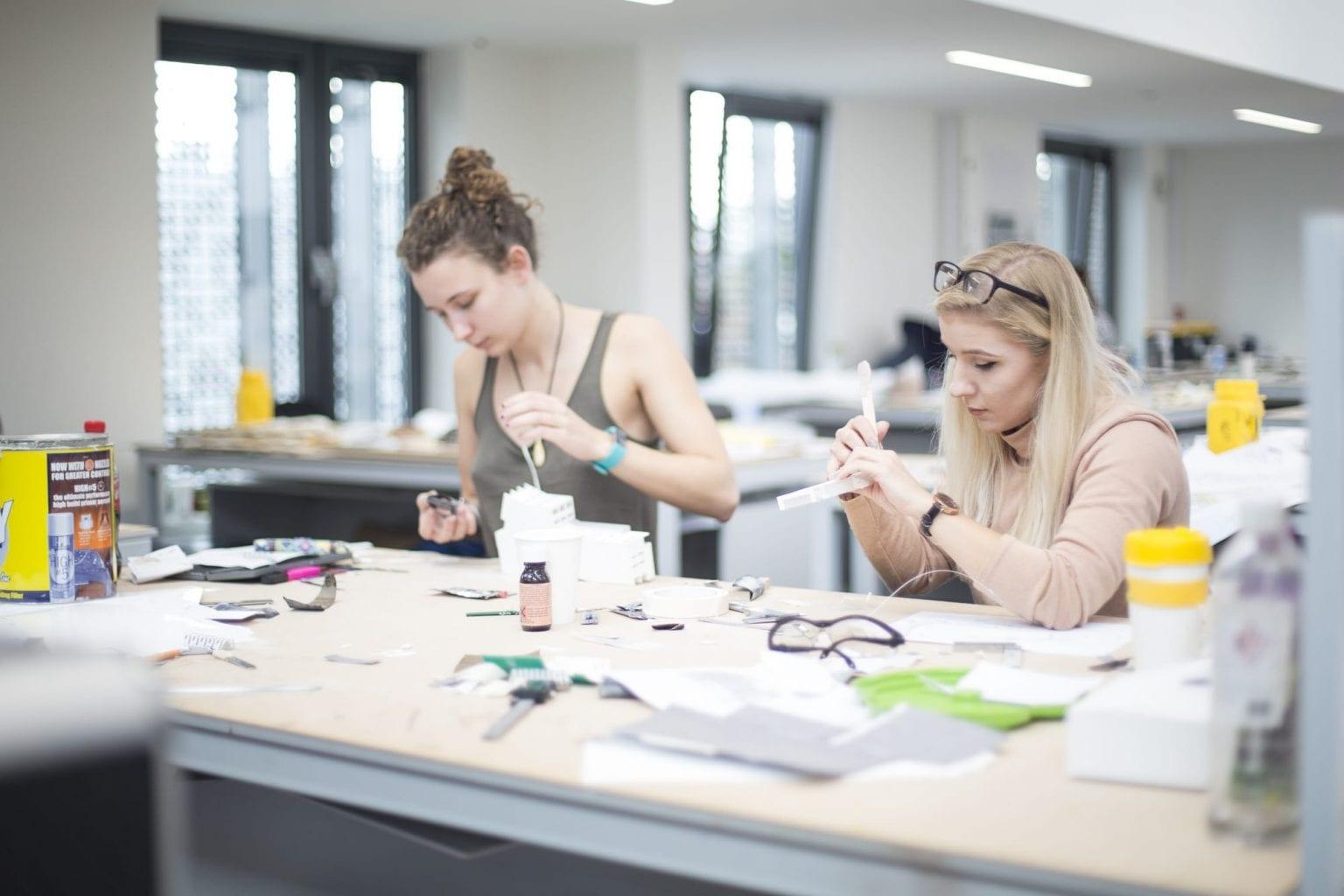 Two people sitting at a table working on modelmaking projects.