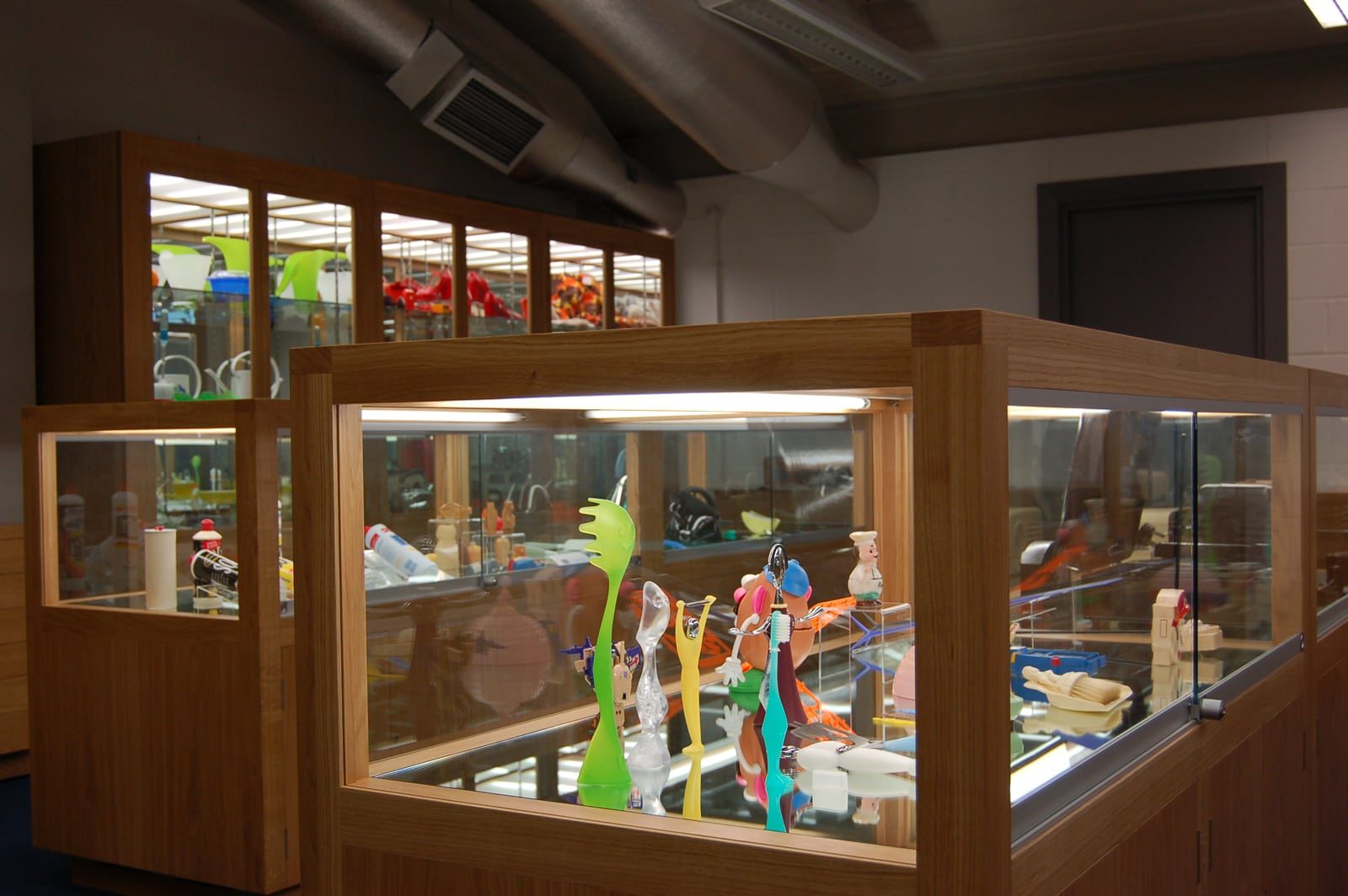 Two wood and glass display cabinets containing plastic exhibits including toys, toothbrushes and kitchen utensils.