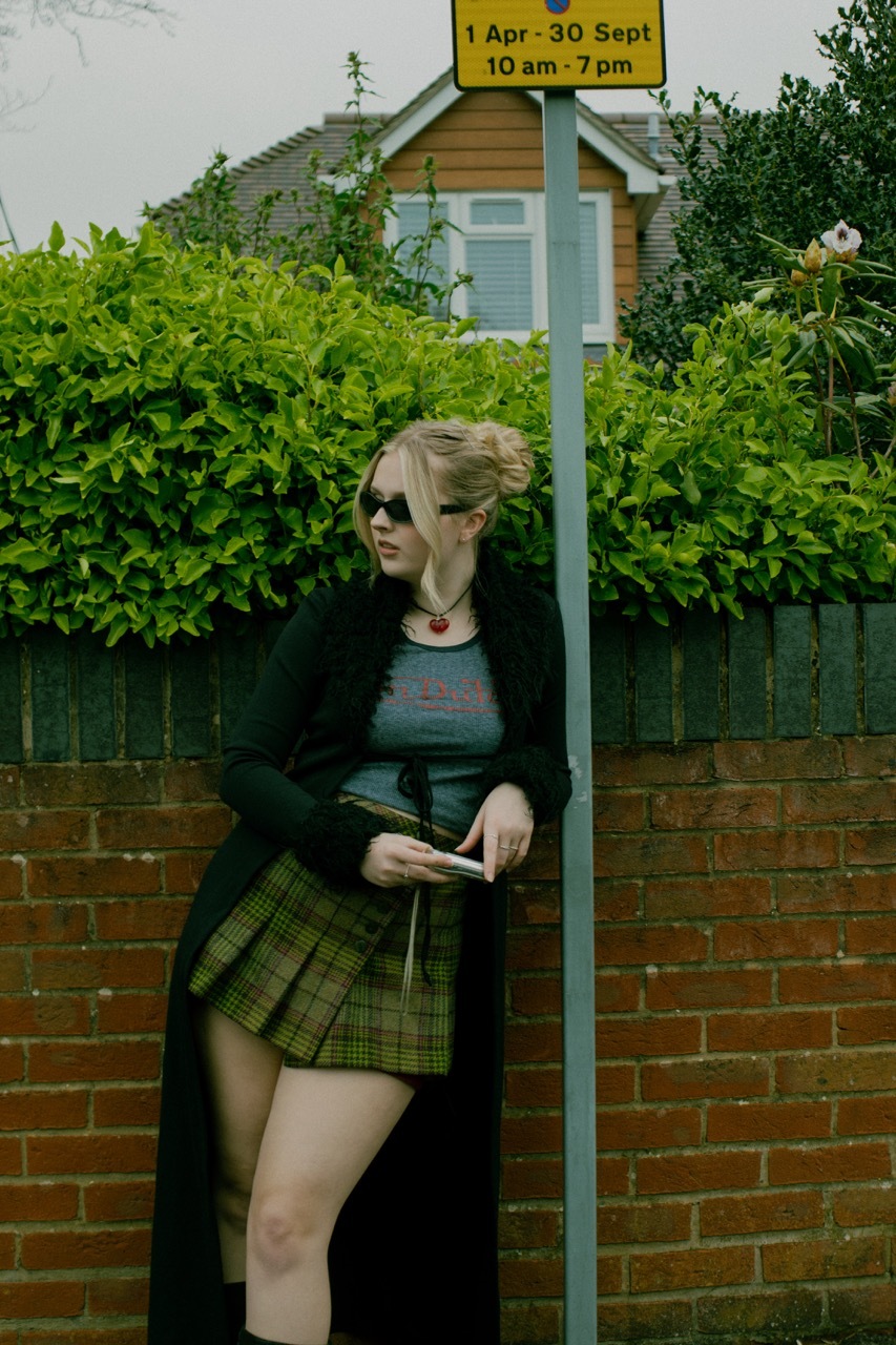 Model stood outside by a sign in front of a wall, unbothered energy, green tint.