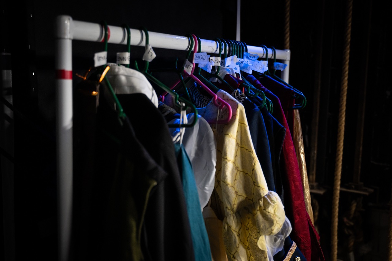 A clothing rail with several garments on colourful hangers, lit from one side against a dark background.