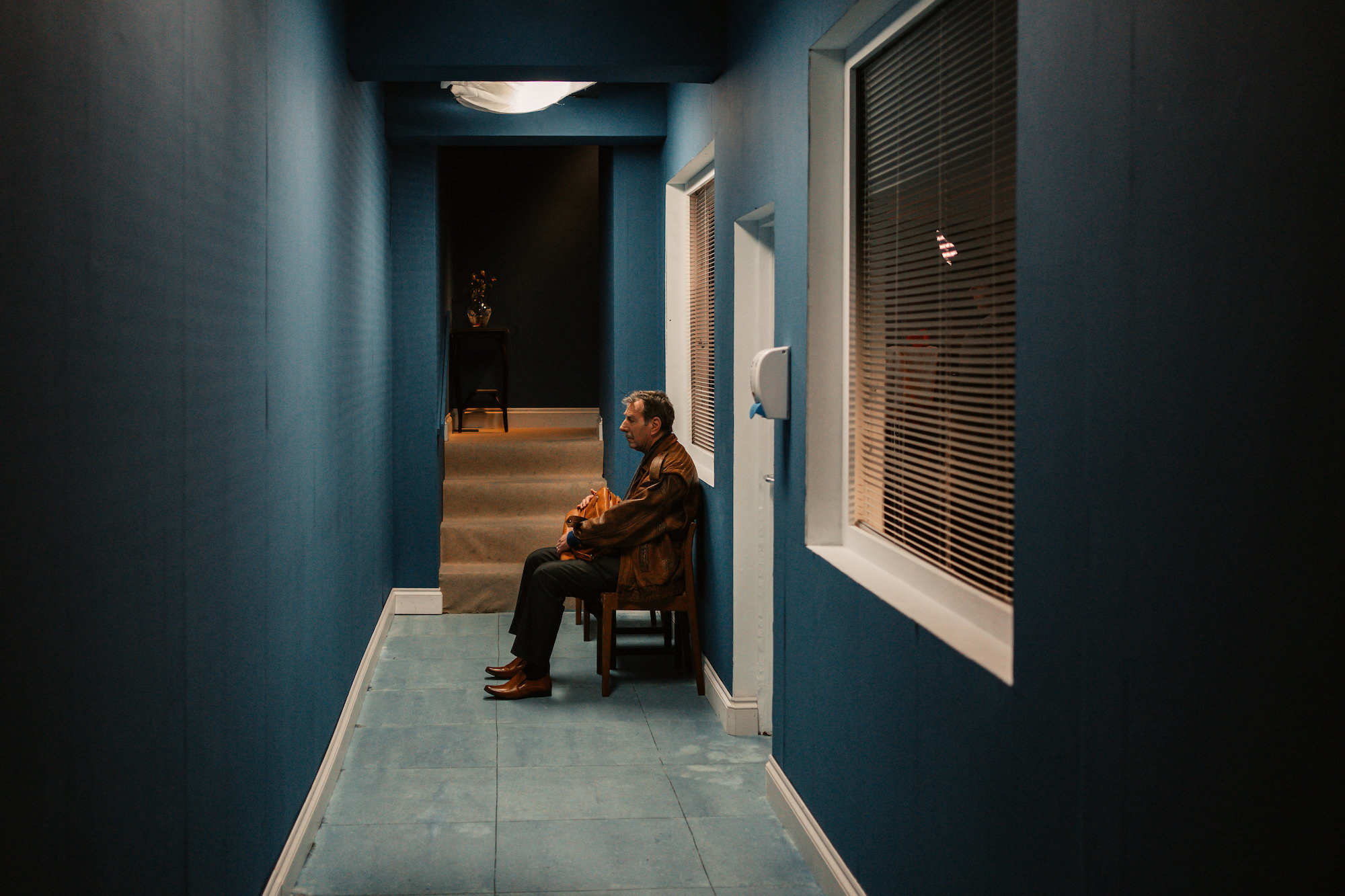 An actor sitting in a corridor outside a morgue in a scene from "Mourning Glories".