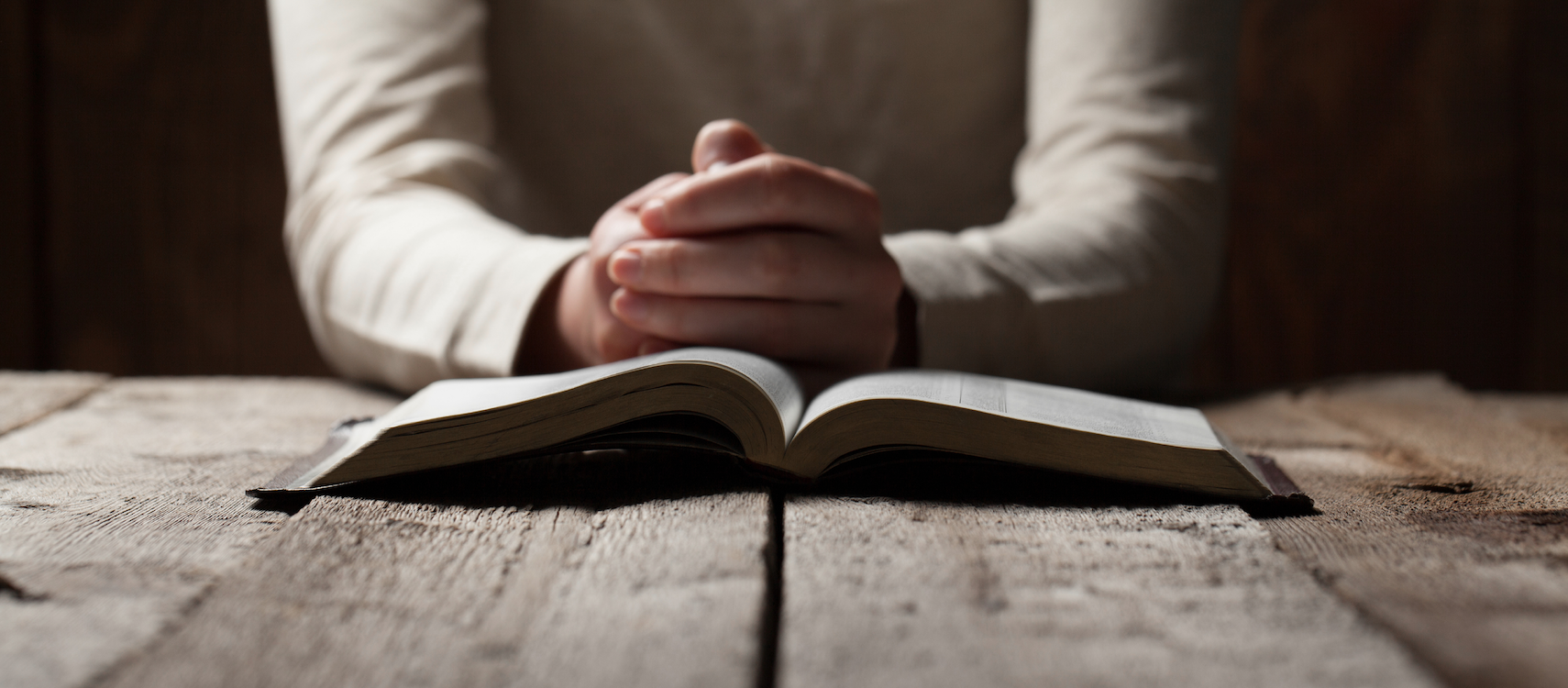 A person putting their hands together in prayer in front of an open Bible.