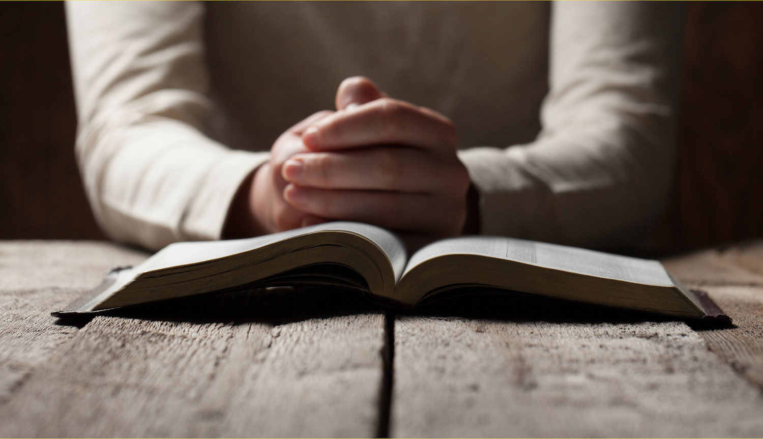Closer image of a person putting their hands together in prayer in front of an open Bible.
