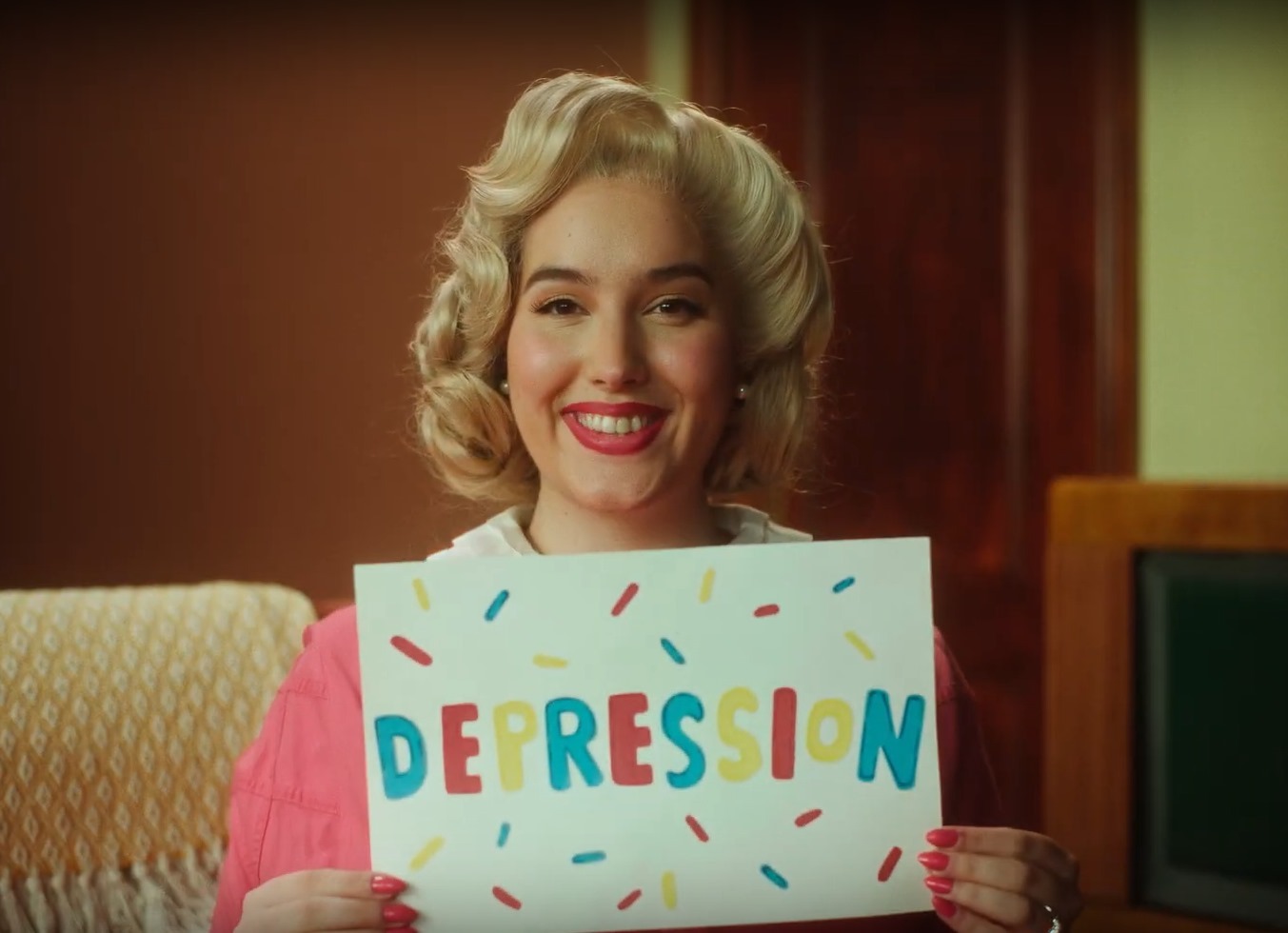 Woman with blonde curled hair holding white sign with "DEPRESSION" in colourful letters and rainbow sprinkles design