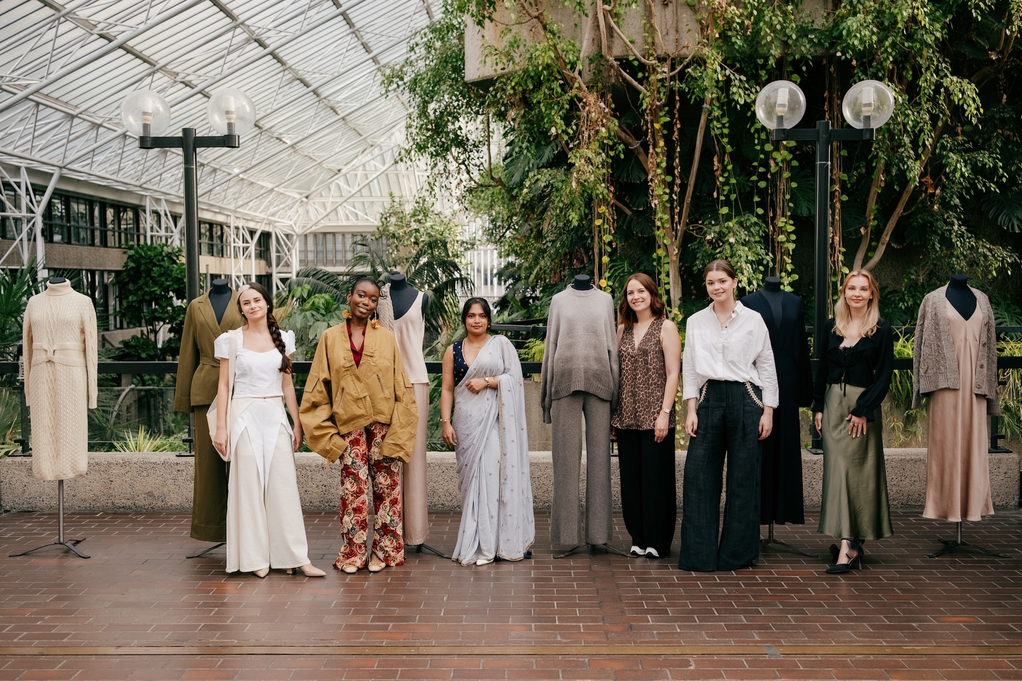 J Horton and five fellow fashion designers standing next to mannequins dressed with woollen garments and posing for a photo at the Net-a-Porter x King's Foundation Barbican launch event.