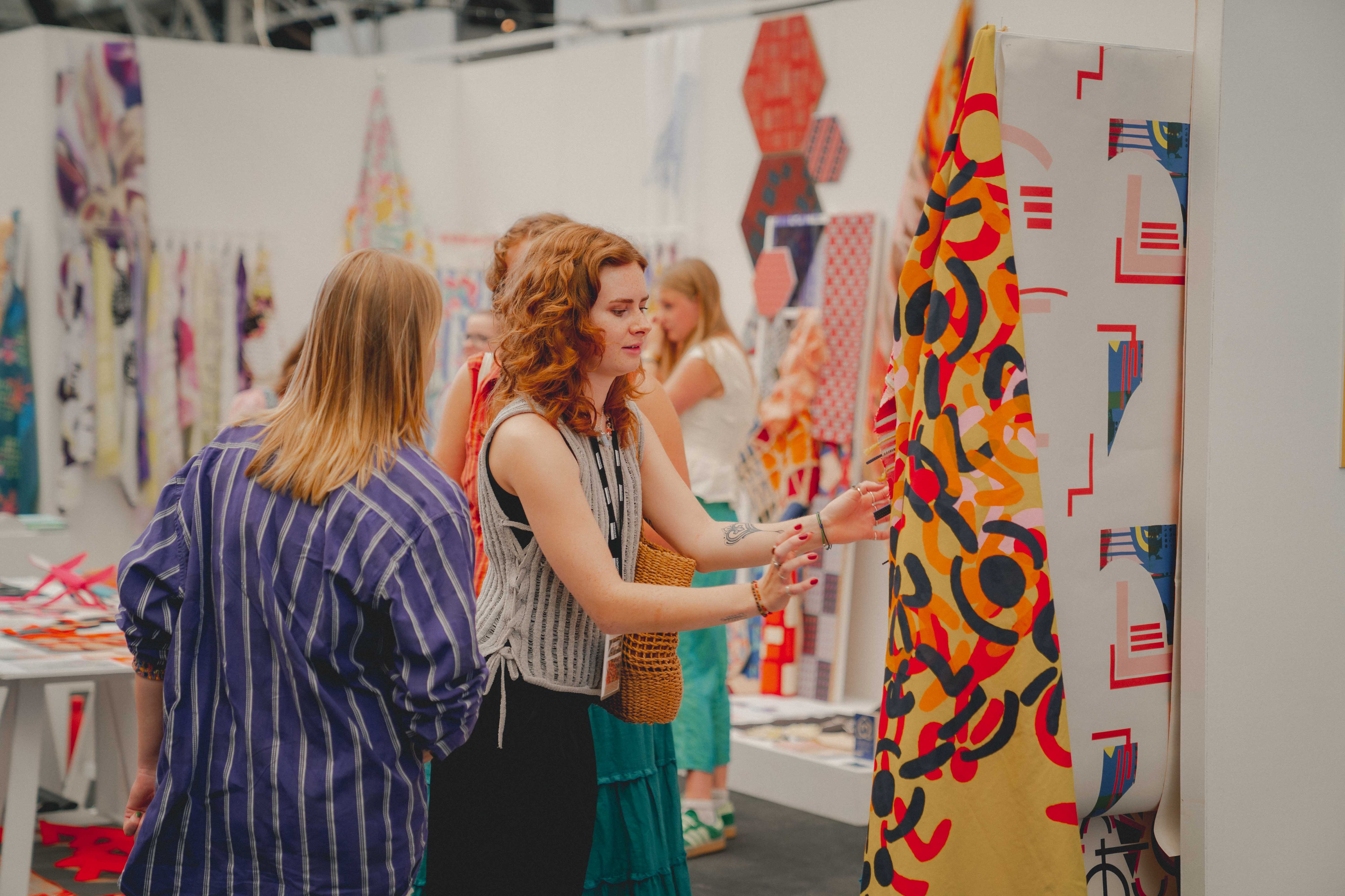 People examining colourful textile displays at trade show with patterned fabrics hanging on white exhibition stands