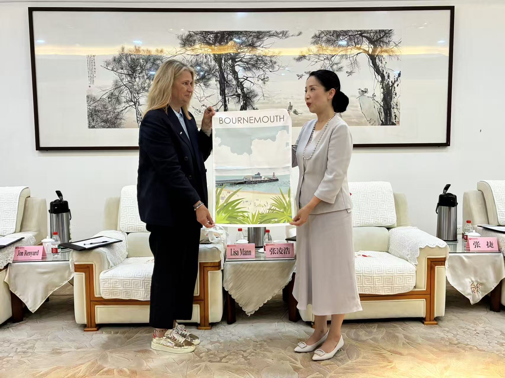 L Mann and a member of the leadership team at Nanjing University of the Arts stand facing each other while holding a poster with an illustration of Bournemouth Pier and the word "Bournemouth" along the top.