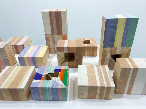 Collection of wooden blocks with coloured stripes in pastel blues, pinks, greens, and browns arranged on white surface.