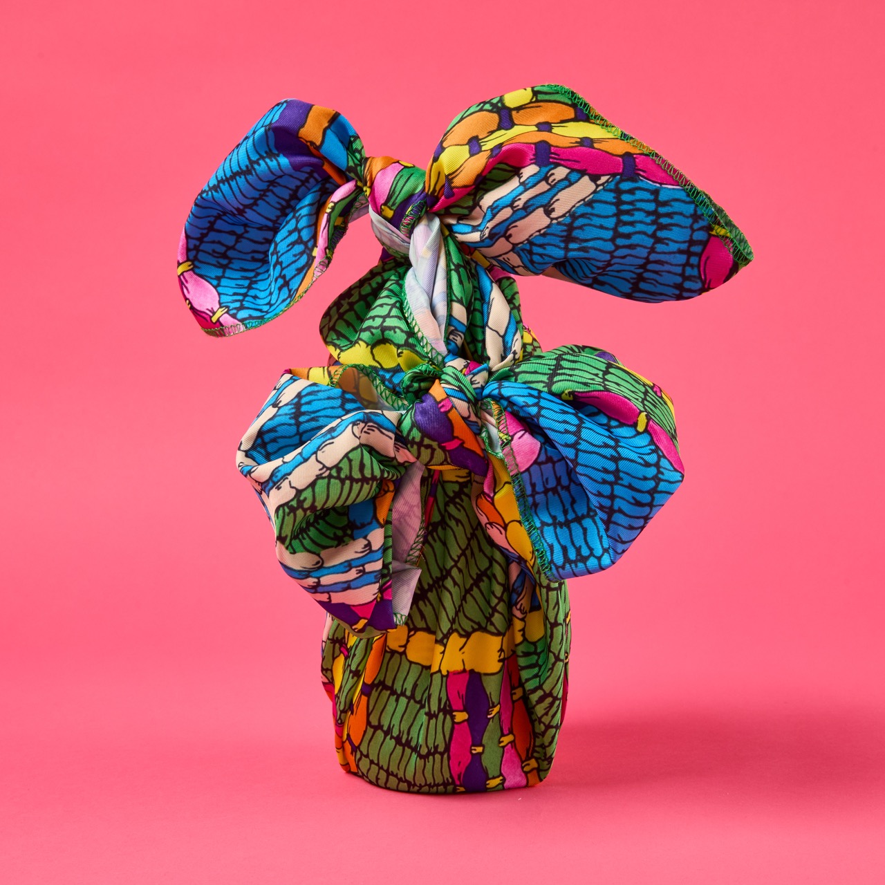 Multicoloured, pattered Lush Knot Wrap on a bright coral pink/red background.